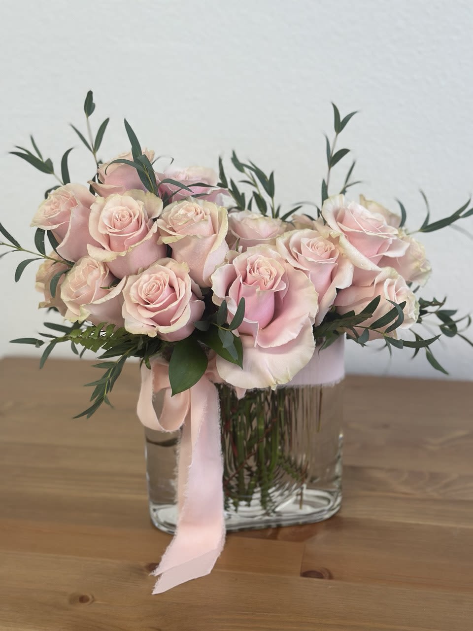 Pink roses arranged in a clear glass vase with a pink ribbon