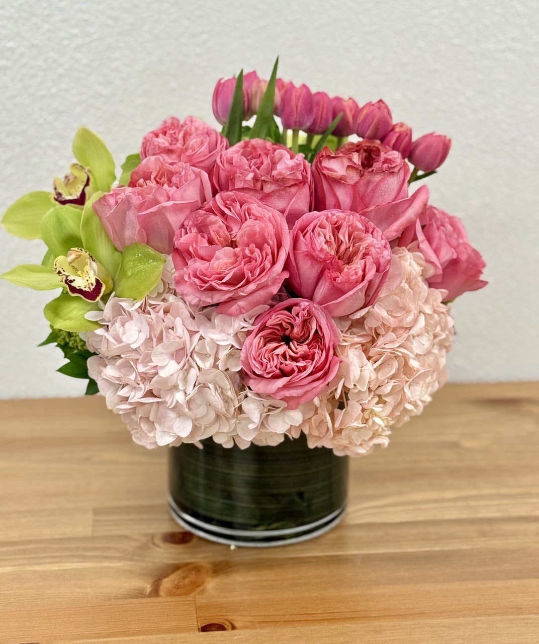 Pink roses and hydrangeas in a black vase with green orchids