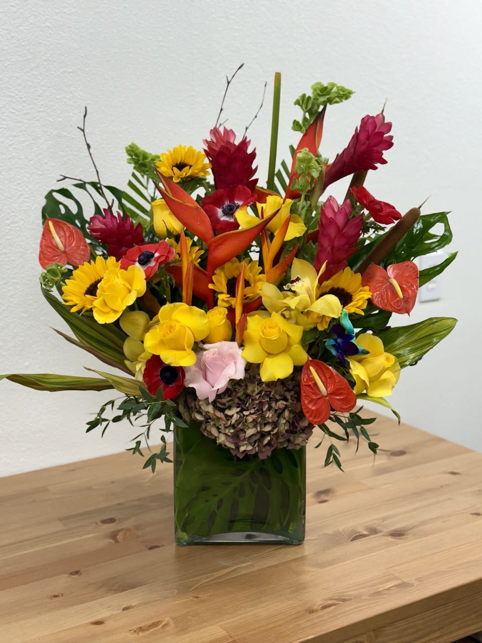 Tropical bouquet with yellow sunflowers and red-orange blooms in a green vase