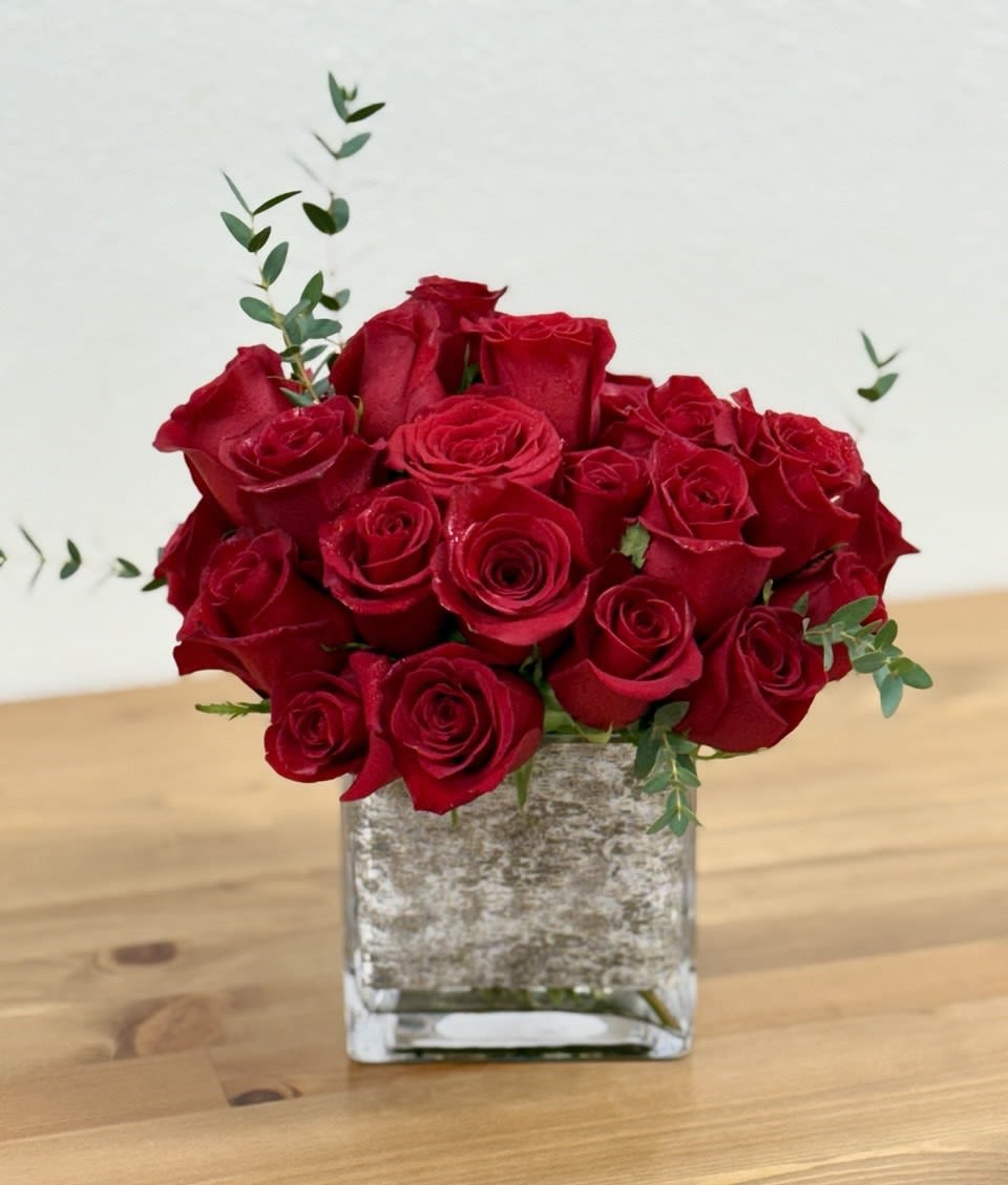 Red roses arranged in a square glass vase with a few eucalyptus stems