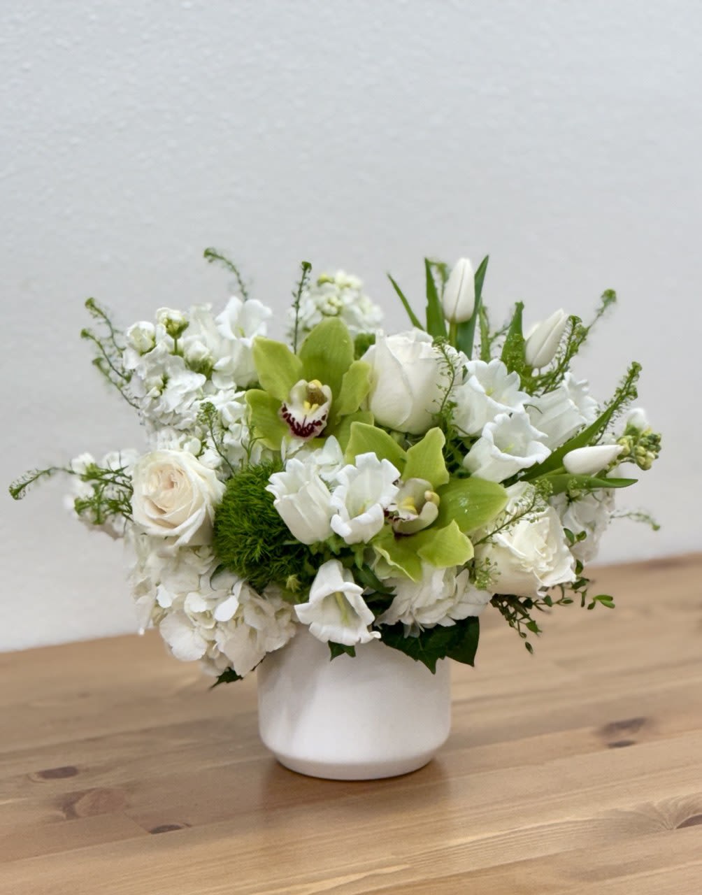 White floral arrangement in a white vase with green orchids and tulips