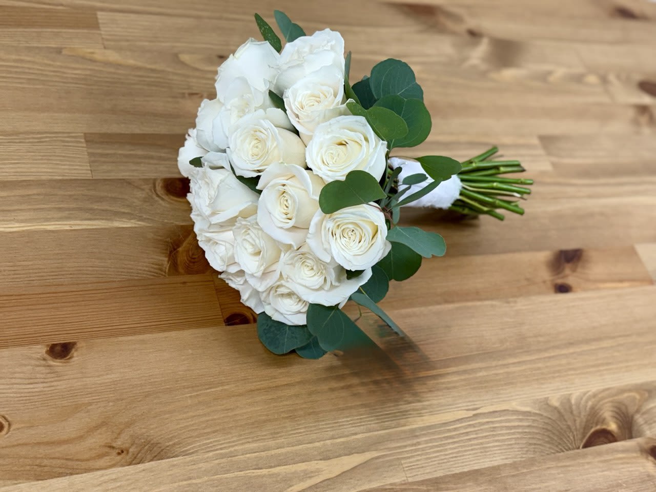 White rose bouquet with green foliage on a wooden surface