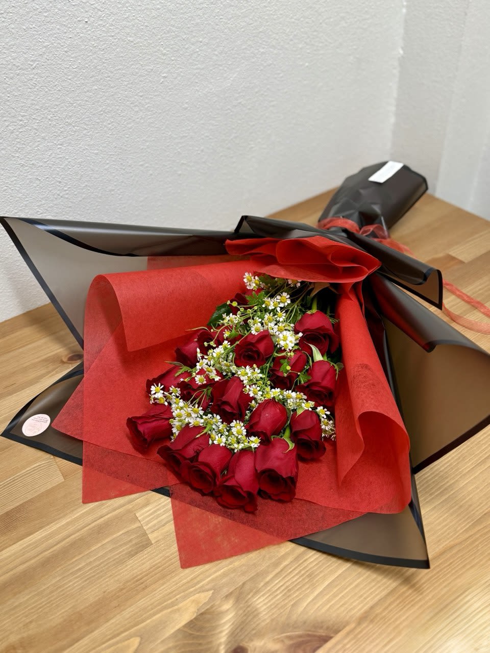 Bouquet of red roses with small white filler flowers in black and red wrap