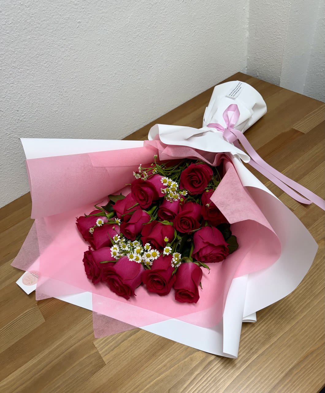 Bouquet of red roses wrapped in pink and white paper with a ribbon