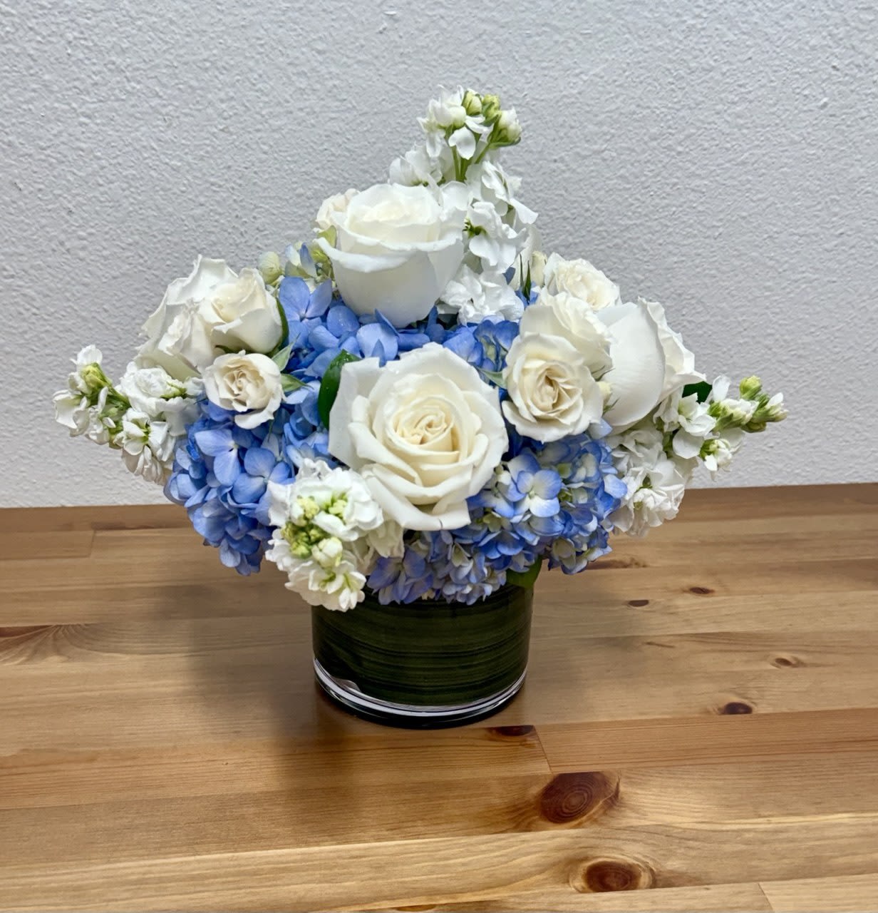 Sky - An elegant arrangement of white and blue flowers, artfully designed with premium blooms and fresh greenery in a glass vase with green liner. The harmonious blend of cool blue tones and pure white blossoms creates a sophisticated, peaceful display suitable for any occasion.