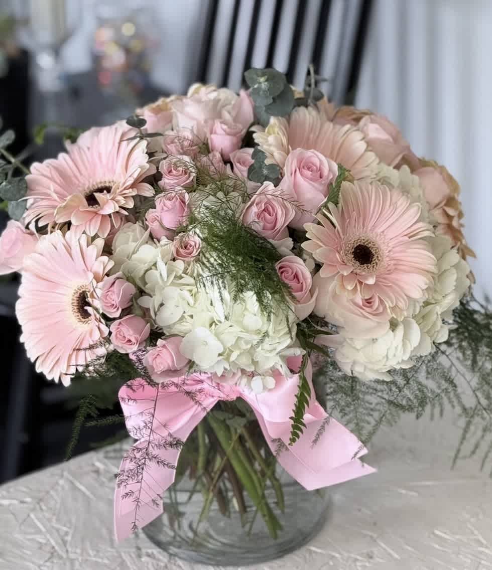 Pink gerbera daisies and roses in a glass vase with a pink ribbon