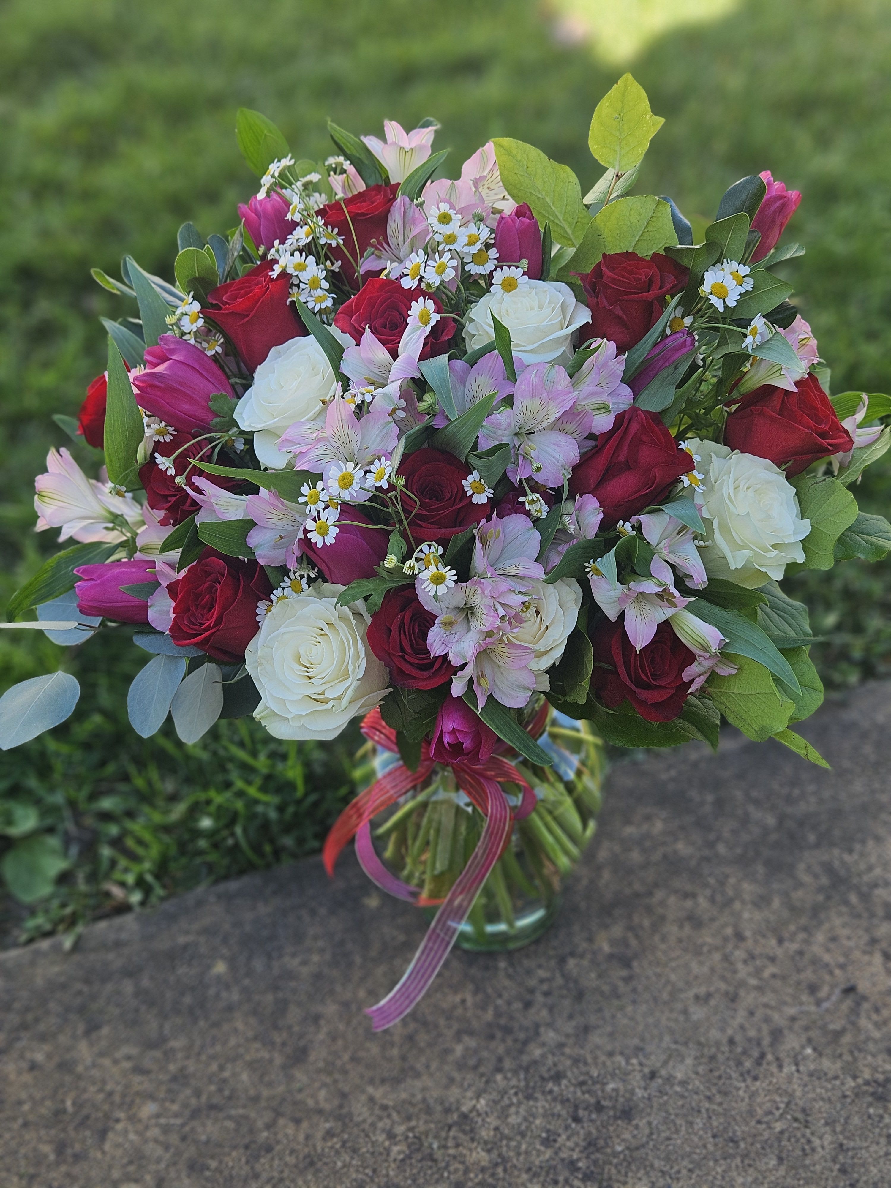 Bouquet of red and white roses with pink alstroemeria and daisies in a glass vase