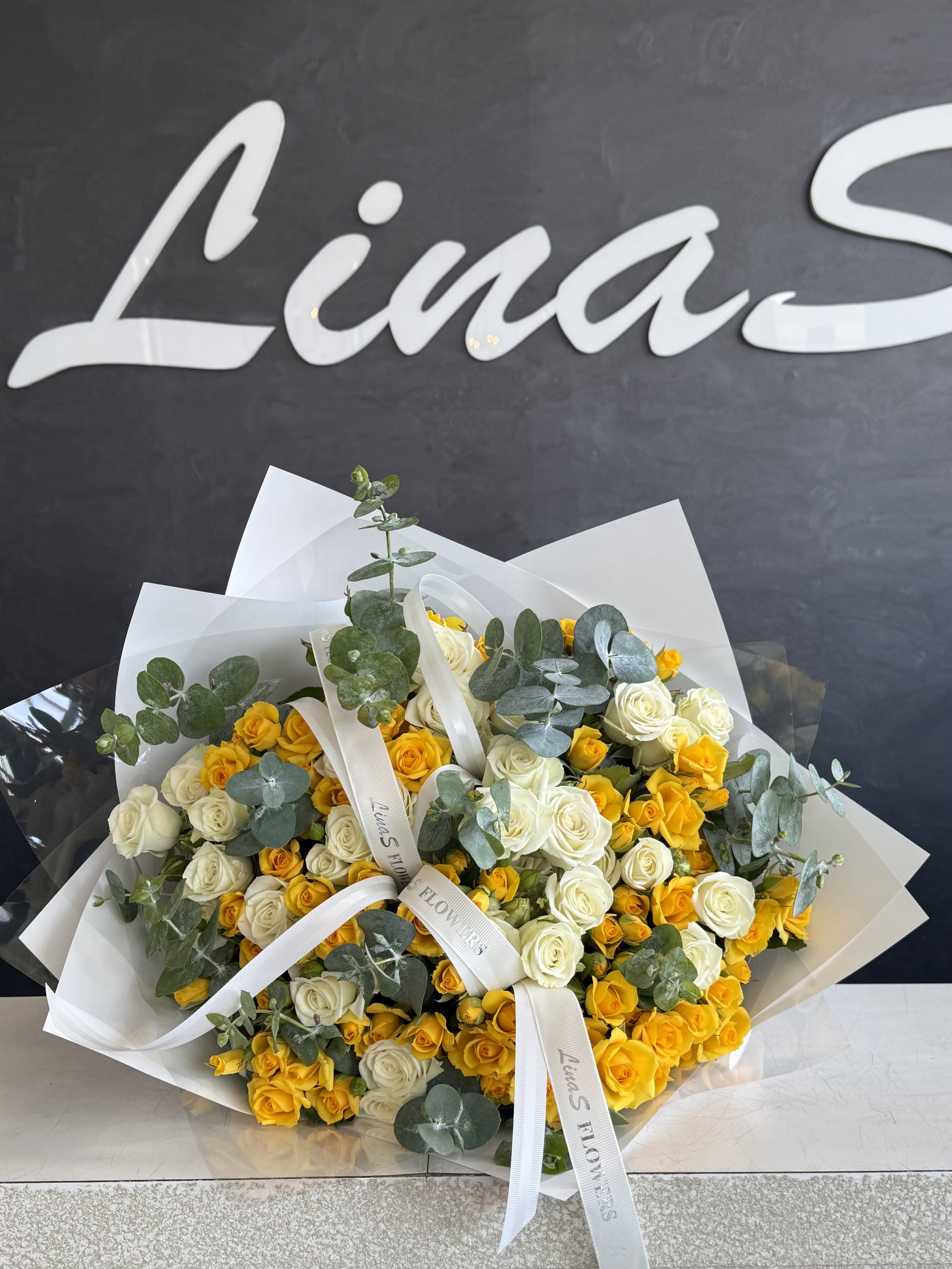 Bouquet of yellow and white roses with eucalyptus in white wrap