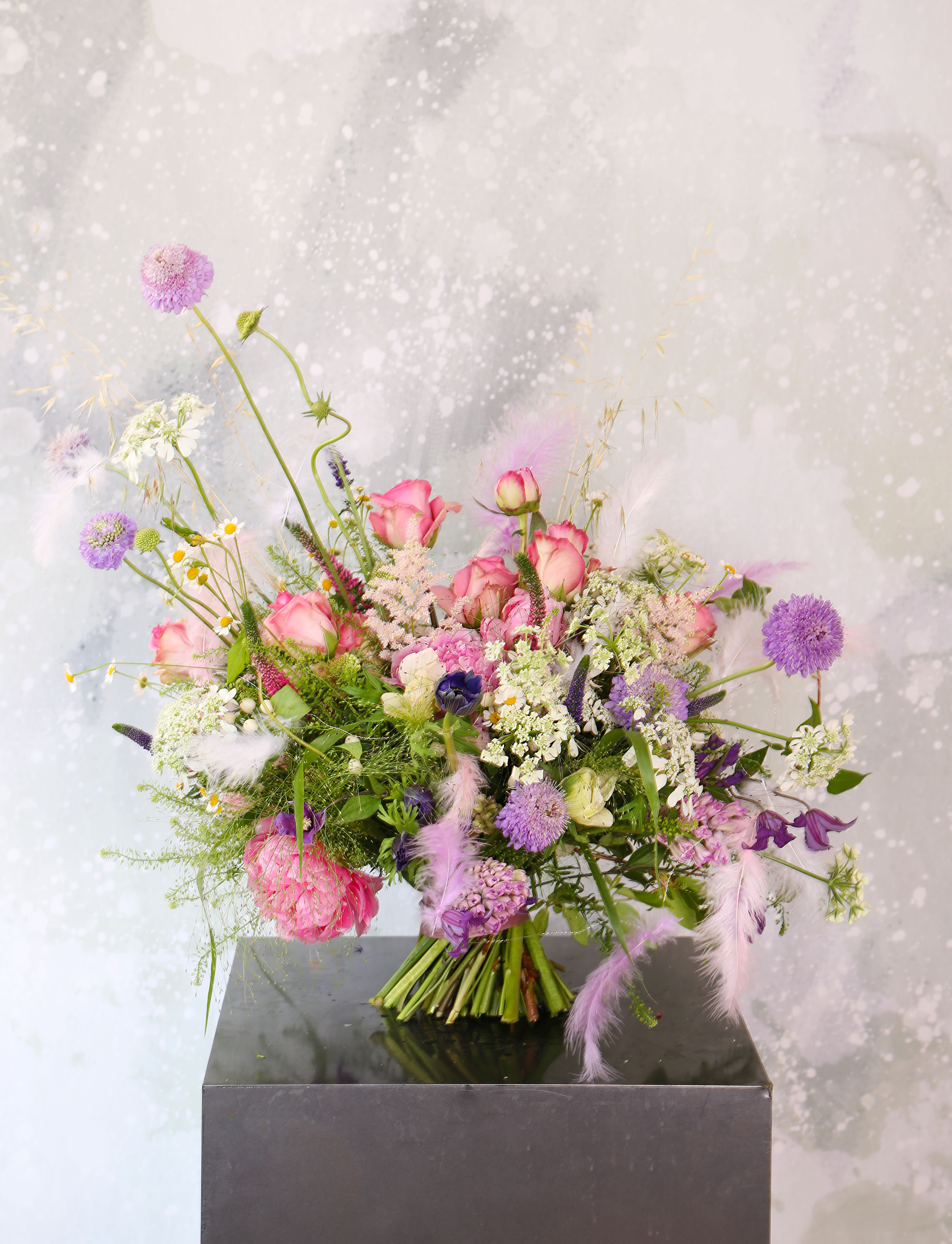 Fireworks - Big variety luxury bloom in this handtie bouquet. Such as Peony, garfen rose, Anemone, Hydrangeas, Hyacinth, scabiosa,Clematis... The hand made feather garland bring in a soft feminine touch and uniqueness.  This handtie bouquet finished in ribbon wrap and comes in 8" round glass round vase Disclaimer: Photo just represent the overall style, look and feel, which may not be able to identically replicate in some instance. We will only substitute item of equal value or higher value. 