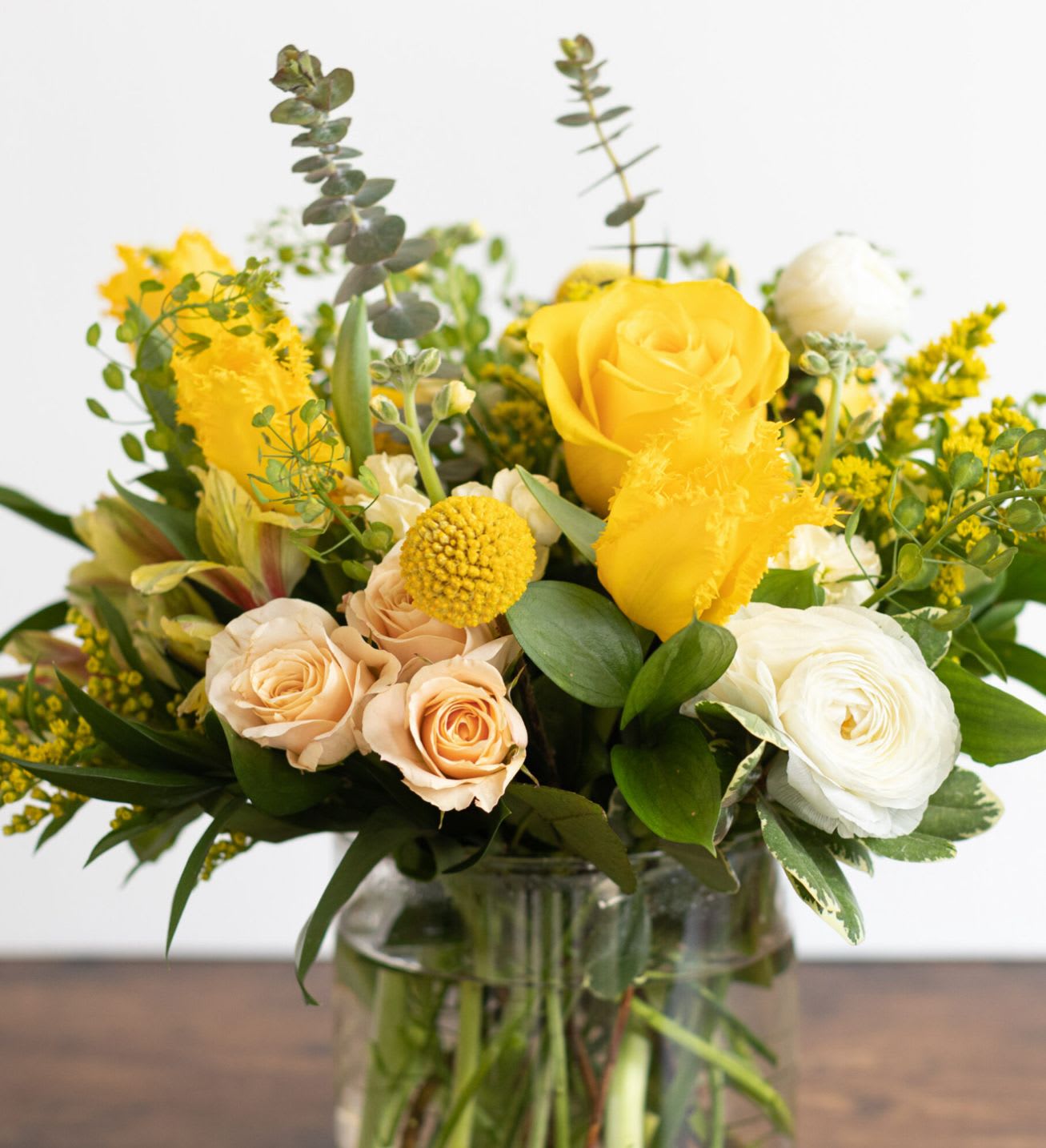 Yellow and cream roses in a glass vase with mixed greenery