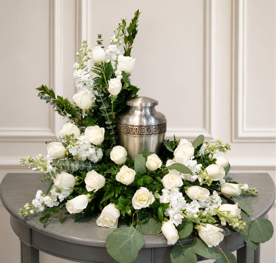 White roses and stock arranged around a silver urn on a table