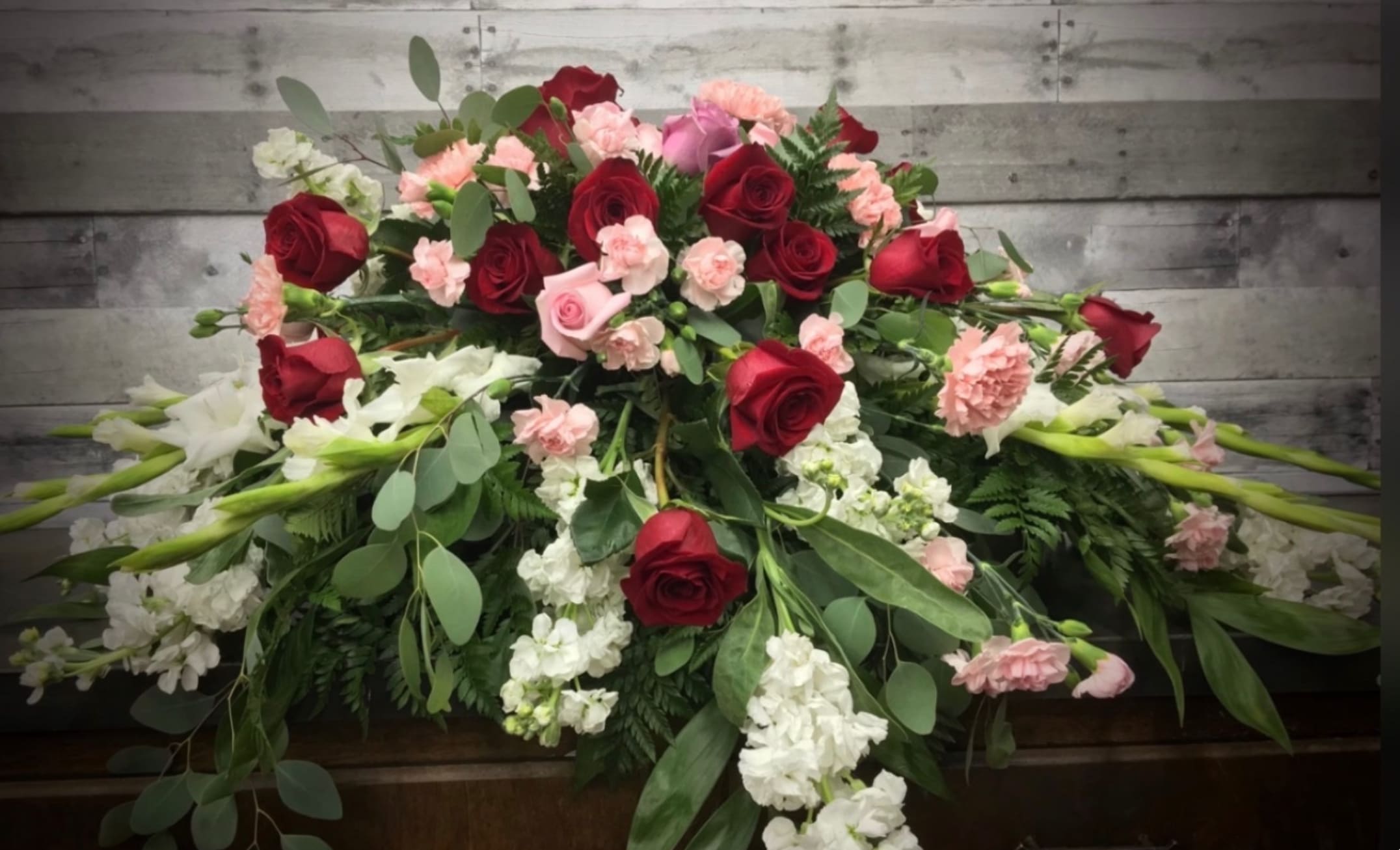 Casket spray with red roses, pink carnations, and white flowers