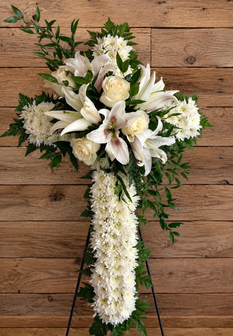 White floral standing spray on an easel with lilies, roses, and chrysanthemums