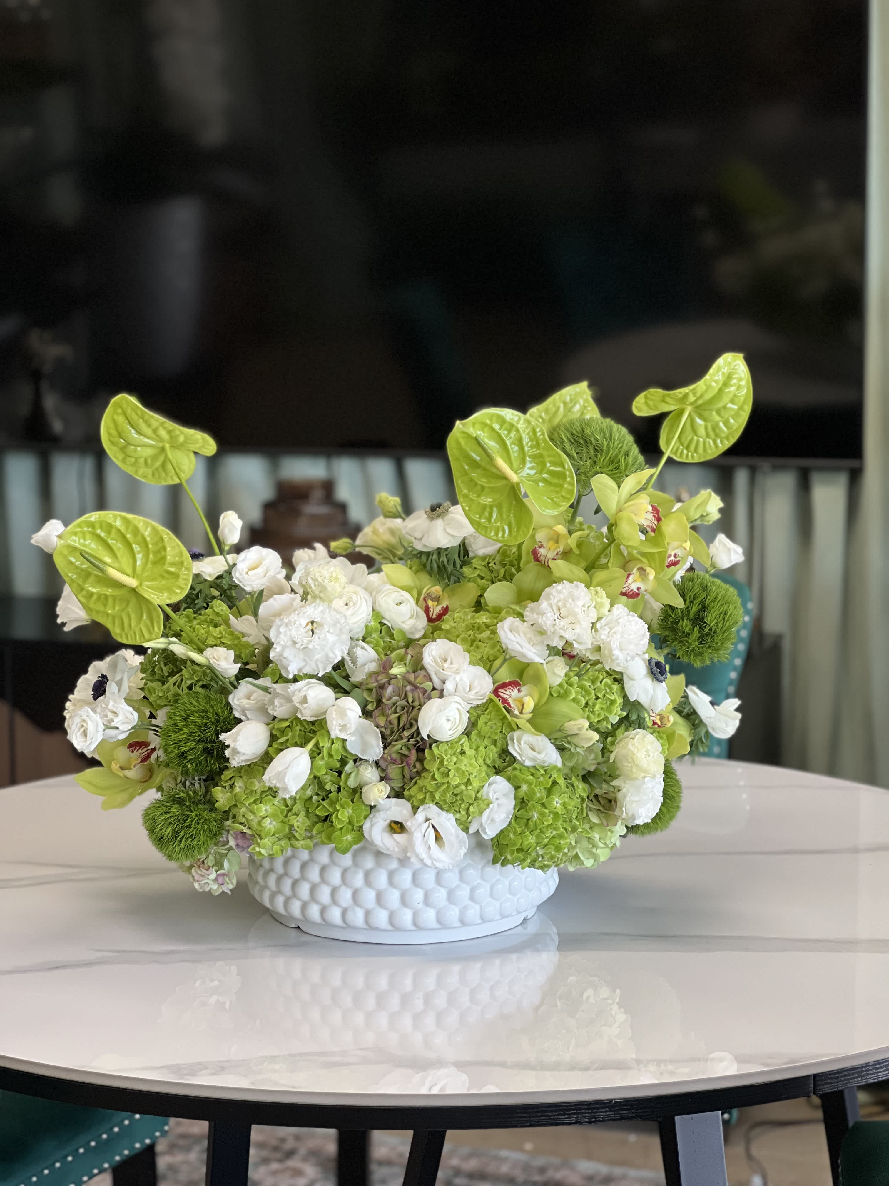 Green and white floral arrangement in a white textured bowl vase
