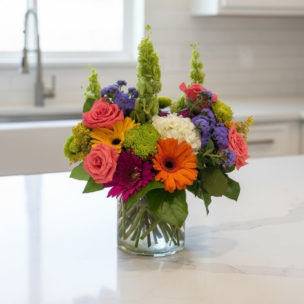 Best Day Ever - A lively celebration of color and texture, this flower arrangement is built to make someone's Best Day Ever - perfect as a birthday bouquet or a bright "just because" surprise. Pink roses and bold orange and magenta gerbera daisies create an immediate burst of joy, while white hydrangea and purple filler blooms add soft contrast so the recipient feels truly seen. Tall green bells of Ireland spikes give the design an energetic, layered silhouette that reads as both festive and modern.  This mixed-color arrangement pairs chrysanthemums, hydrangeas, gerbera daisies, roses and bells of Ireland  in a dense, rounded composition set in a clear glass vase that keeps the look clean and lets stems show for a fresh, garden-picked feel. Green button mums and other small accents add playful texture; the overall size and fullness make it a generous centerpiece or bedside pick-me-up. It's an ideal choice for saying thank you, sending get-well wishes, congratulating someone, or celebrating Mother's Day - and it's equally at home as a summer-ready gift to lift spirits any time of year. Care: keep fresh water in the vase and trim stems occasionally to prolong bloom life.