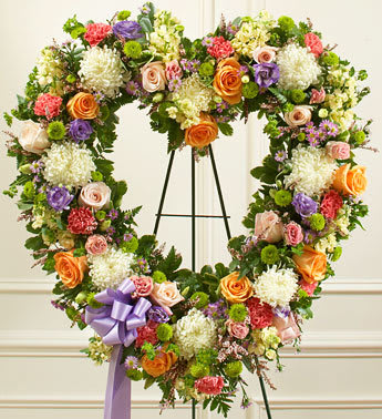 Heart-shaped floral wreath with roses, carnations, and a purple ribbon