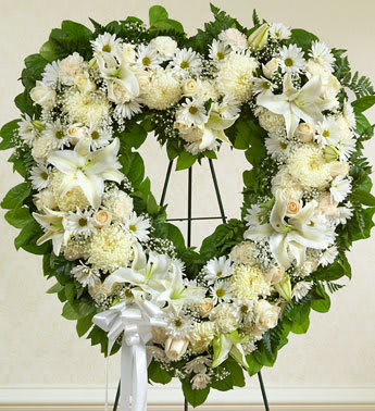 Heart-shaped white floral wreath on a stand with a white ribbon