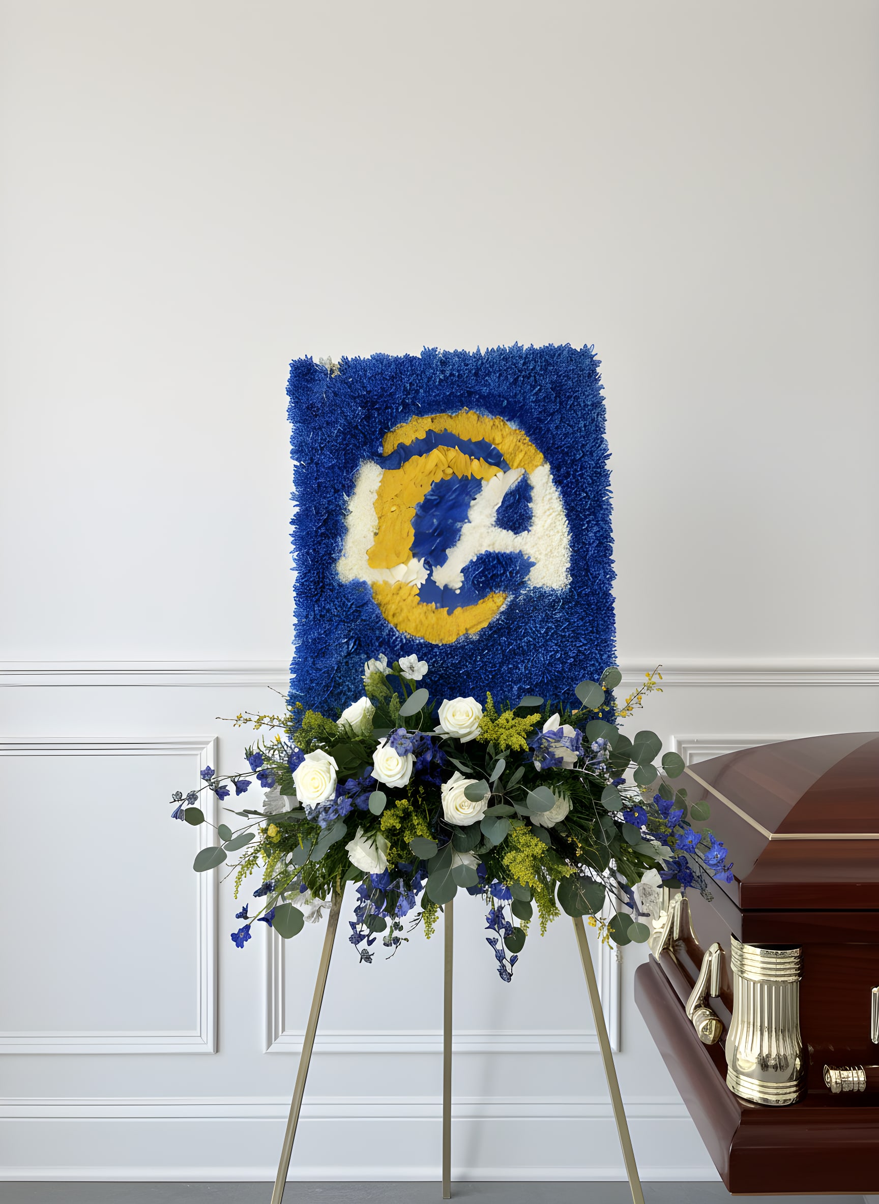 Blue and yellow floral funeral tribute on an easel beside a casket
