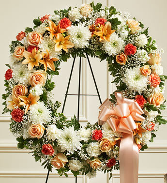 Floral wreath with peach roses, white mums, and orange lilies on an easel