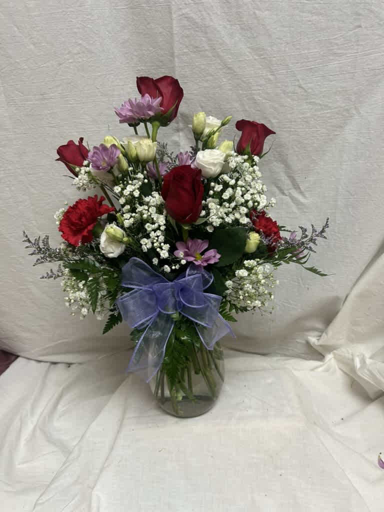 Mixed bouquet of red roses, white blooms, and purple flowers in a glass vase