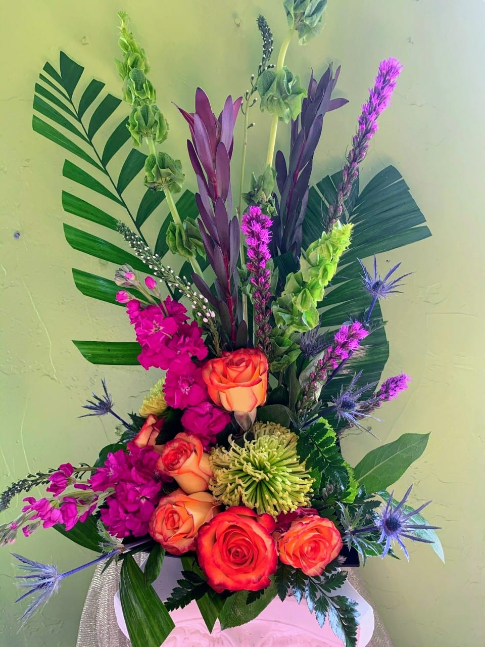 Tall tropical bouquet with orange roses, magenta blooms, and purple accents