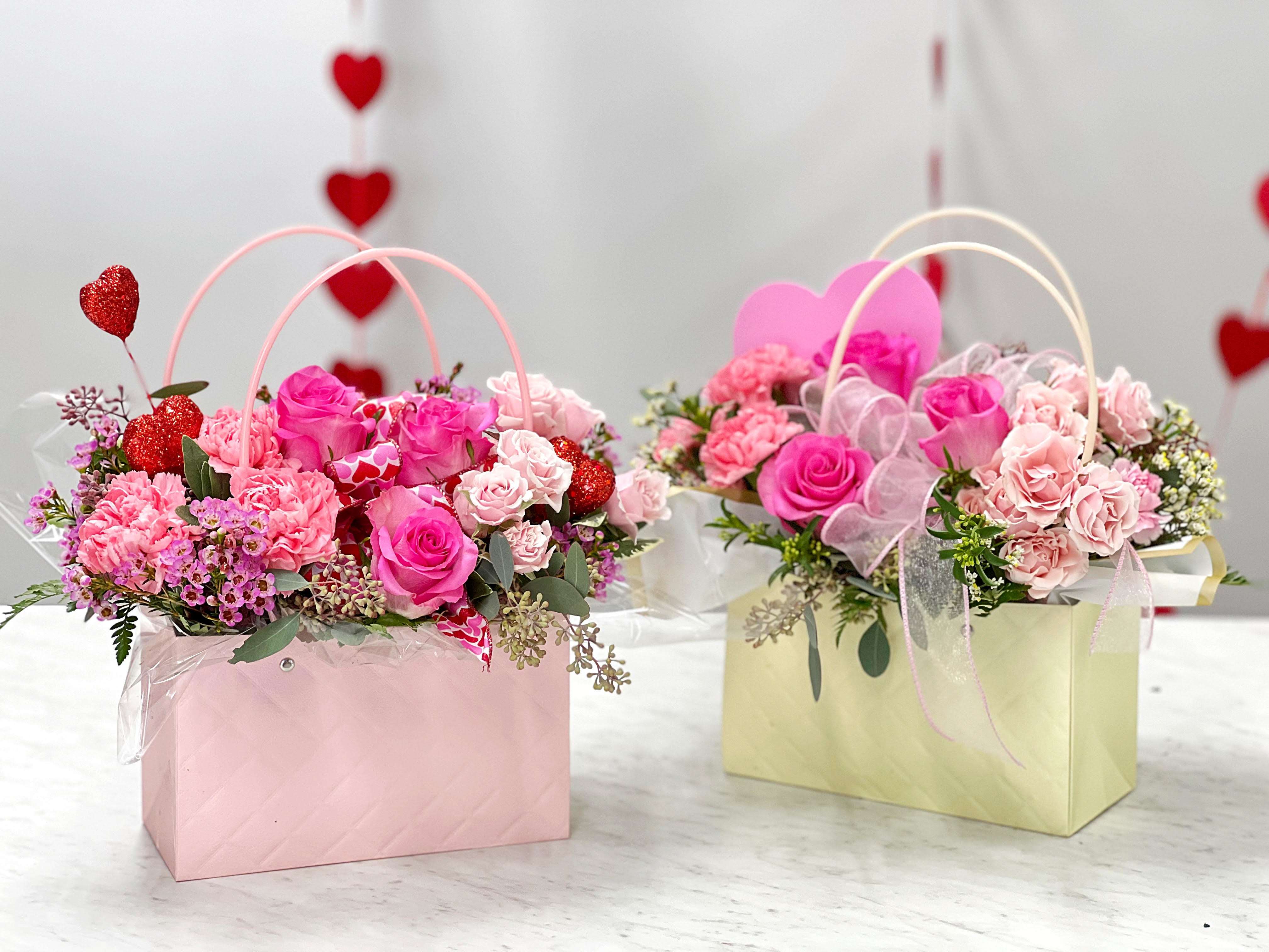 Two pink floral gift baskets with roses and carnations, decorated with heart picks