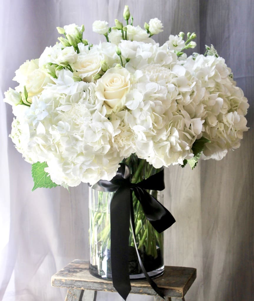 White hydrangea and rose arrangement in a clear glass vase with a black ribbon