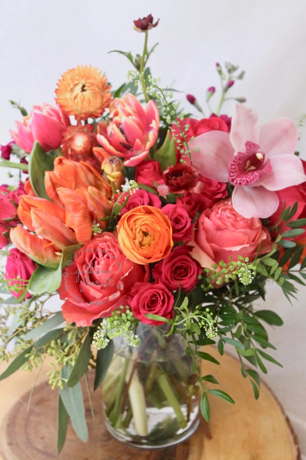 Mixed bouquet of pink, orange, and red flowers in a glass vase