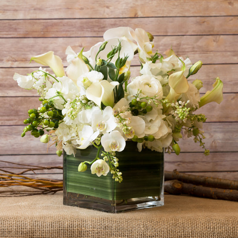 PURE FEELINGS - ELEGANT ROMANTIC VISION IN A GLASS CUBE WITH WHITE PHALAENOPSIS ORCHID, WHITE CALLA LILIES, WHITE SWEET PEAS, WHITE RANANCULUS, WHITE LILAC, WHITE HYDRANGEAS, WHITE LISIANTHUS, AND GREEN HYPERICUM.  