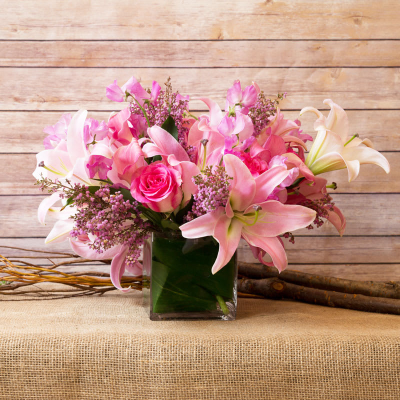 TOUCH OF LOVE  - REMINISCE WITH THIS MIX OF PINK SHADES, LILIES, PINK MALIBU ROSES, PINK CALLA LILIES, SWEET PEAS, AND HEATHER IN A GLASS CUBE LINED WIT GREEN LEAF INSIDE.