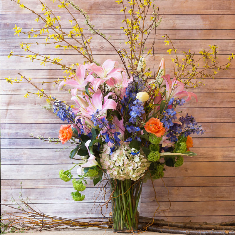 SECRET SPRING GARDEN  - RADIANT GARDEN MIX WITH ORANGE ROSES, ANTIQUE HYDRANGEAS, VIBURNUM HYDRANGEAS, PINK STARGAZER LILIES, BLUE DELPHINIUMS, FRENCH WHITE TULIPS, AND FORSITIA BRANCHES. 