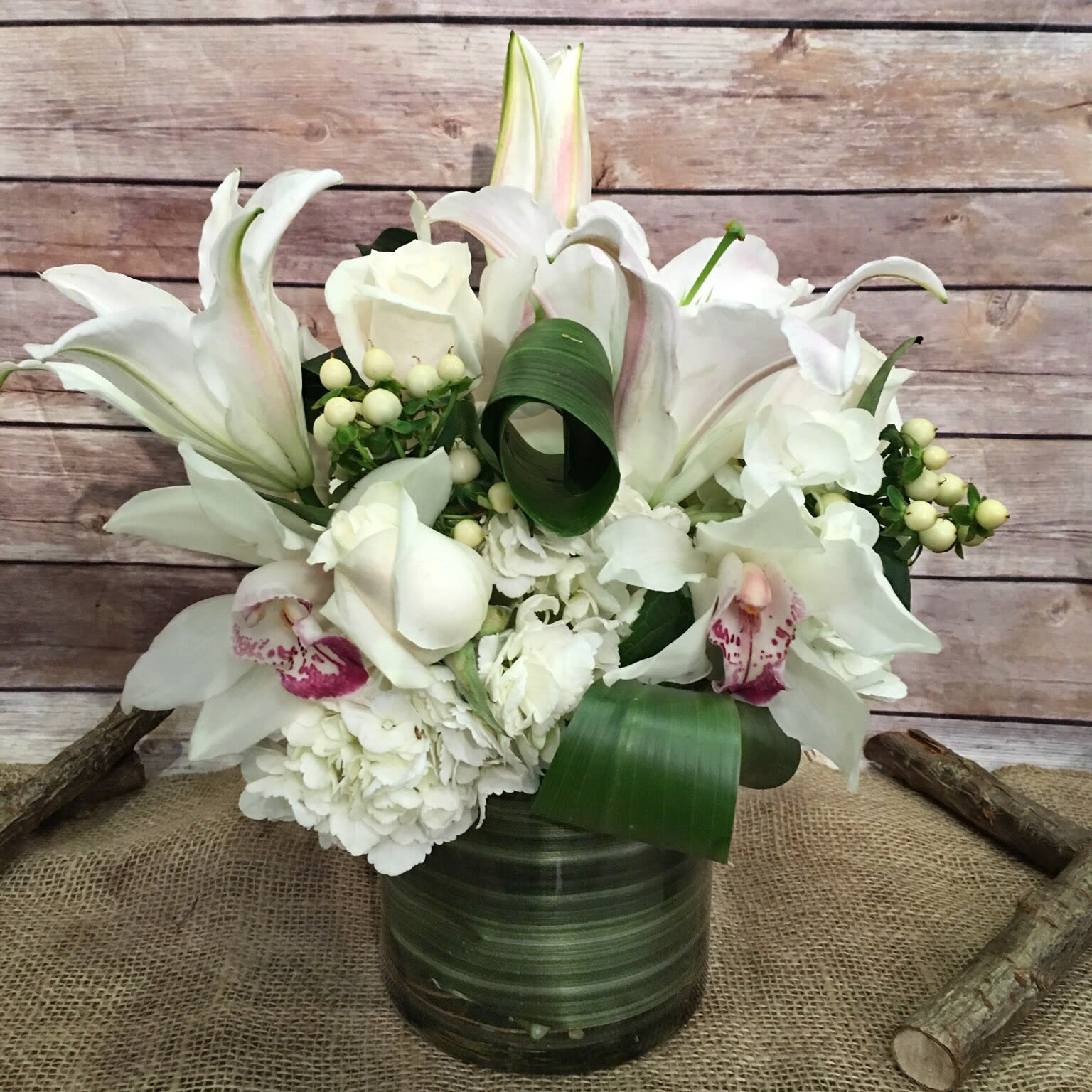 ELEMENTS OF PEACE  - PEACEFUL ASSORTMENT OF WHITE CASABLANCAS LILYS, WHITE HYDRANGEAS, WHITE HYPERICUM, WHITE ROSES, AND WHITE CYMBIDIUM ORCHIDS, IN SMALL GLASS CYLINDER.