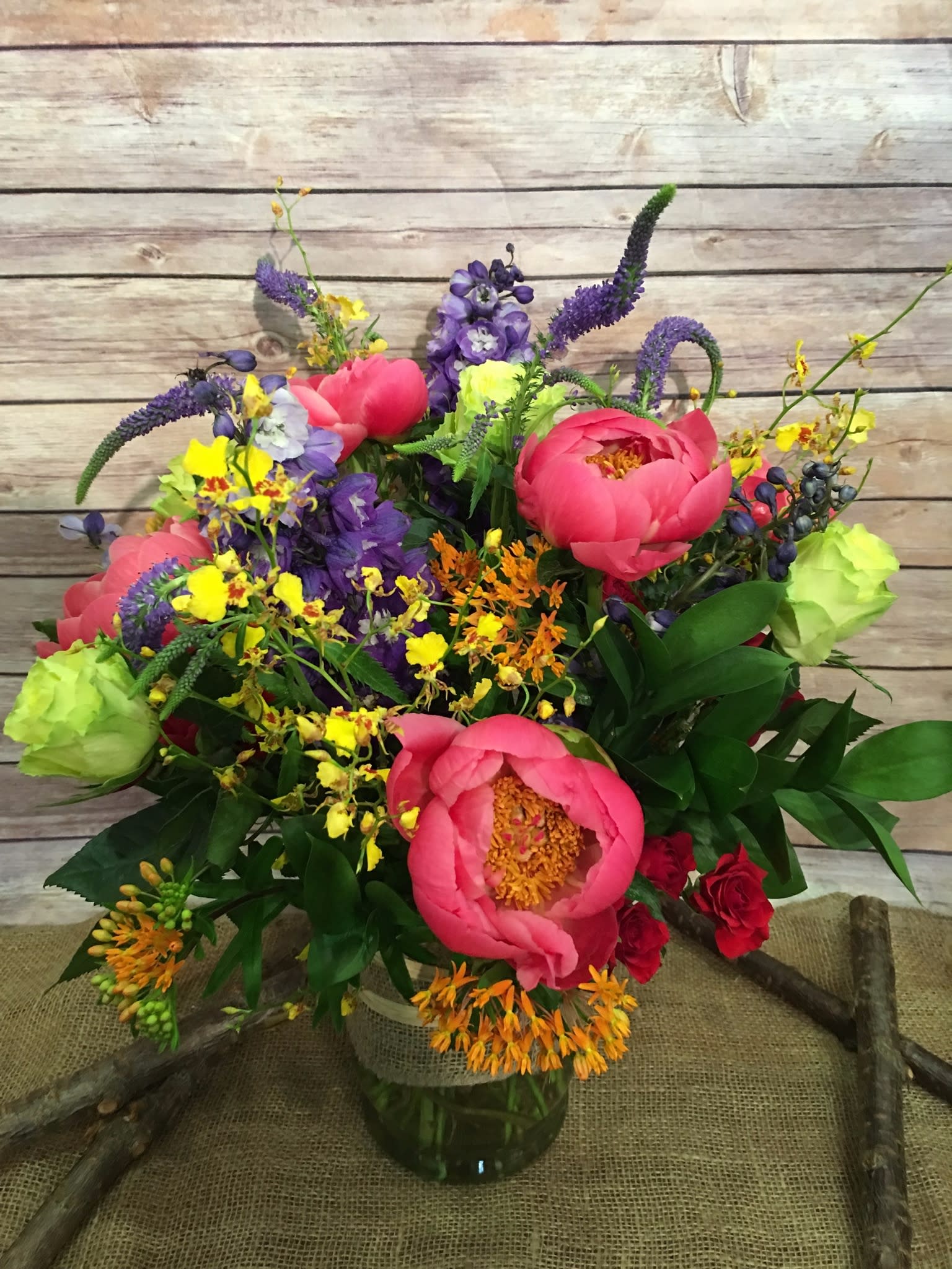 BLAZING SUMMER  - SUTTLE ASSORTMENT OF BRIGHT AND LUSH FLOWERS. CORAL CHARM PEONIES, GREEN ROSES, PURPLE VERONICA, RED SPRAY, BLUE DELPHINIUM, AND YELLOW ONCIDIUM IN VASE. 