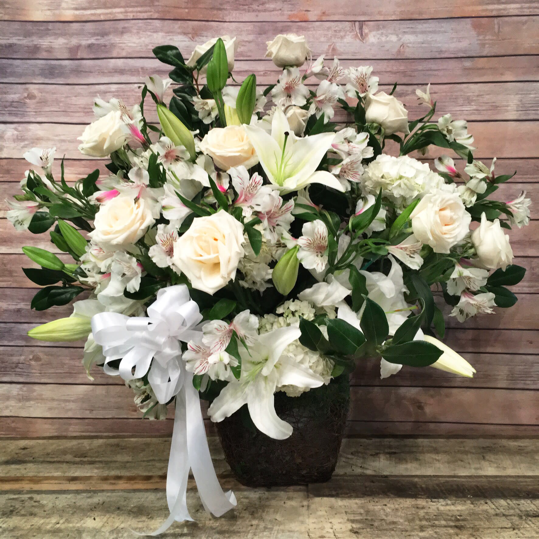 GARDEN FUNERAL FLOOR BASKET  - MIX ASSORTMENT OF WHITE ROSES, WHITE LILIES, WHITE ALSTROEMERIA, CAMELLIA BRANCHES.  (CAN BE REQUESTED IN ANY OTHER COLOR NEEDED OR ON A STANDING BASKET)