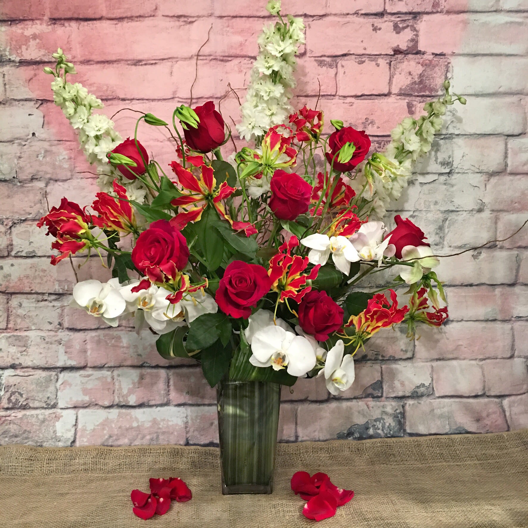 MAISON DES FLEURS - Roth child lily (Japanese Gloriosa)Hybrid delphinium white, red roses, phaleonopsis white, accented with touch of curly willow.