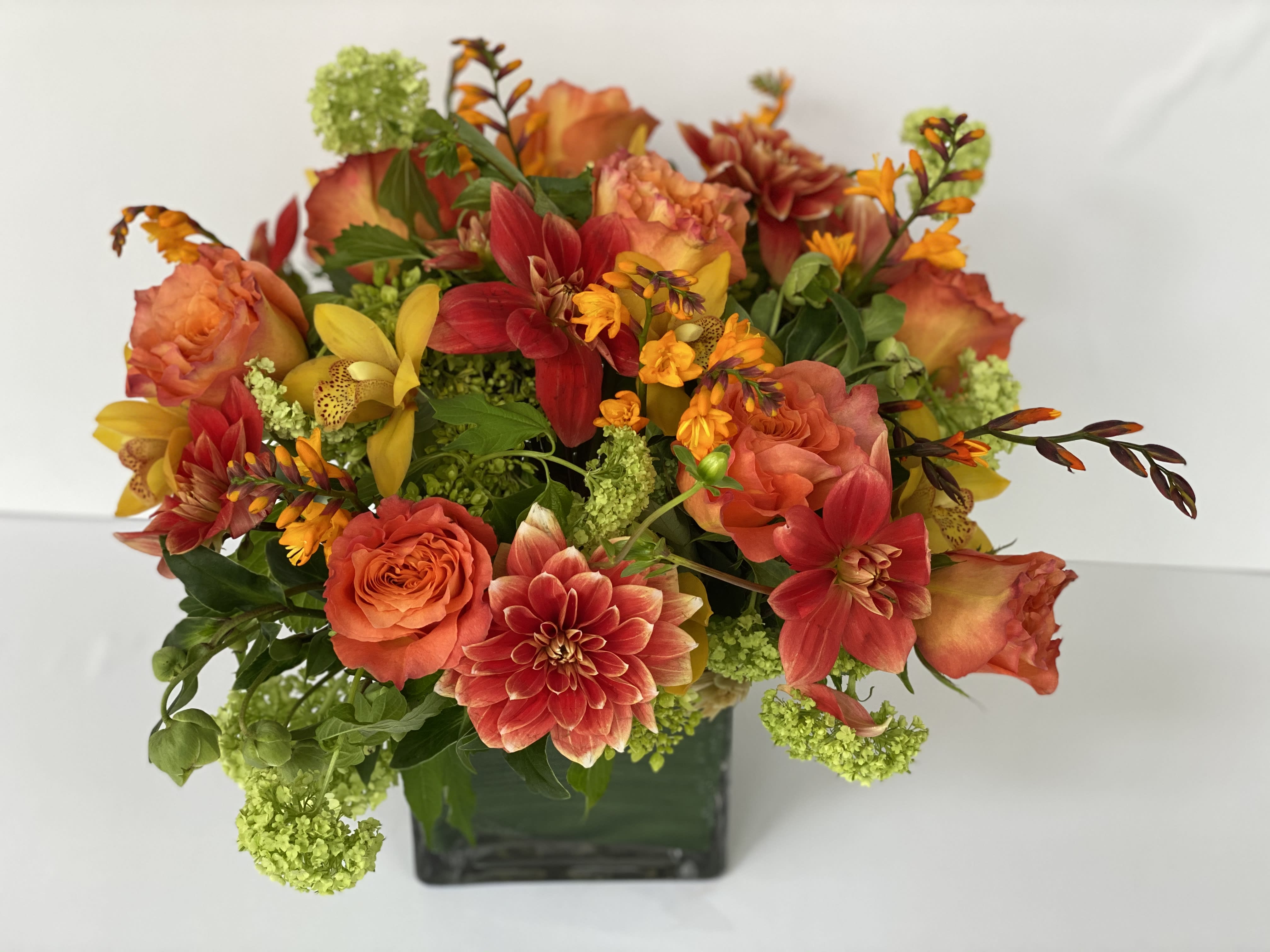 Orange and red mixed flowers arranged in a square glass vase