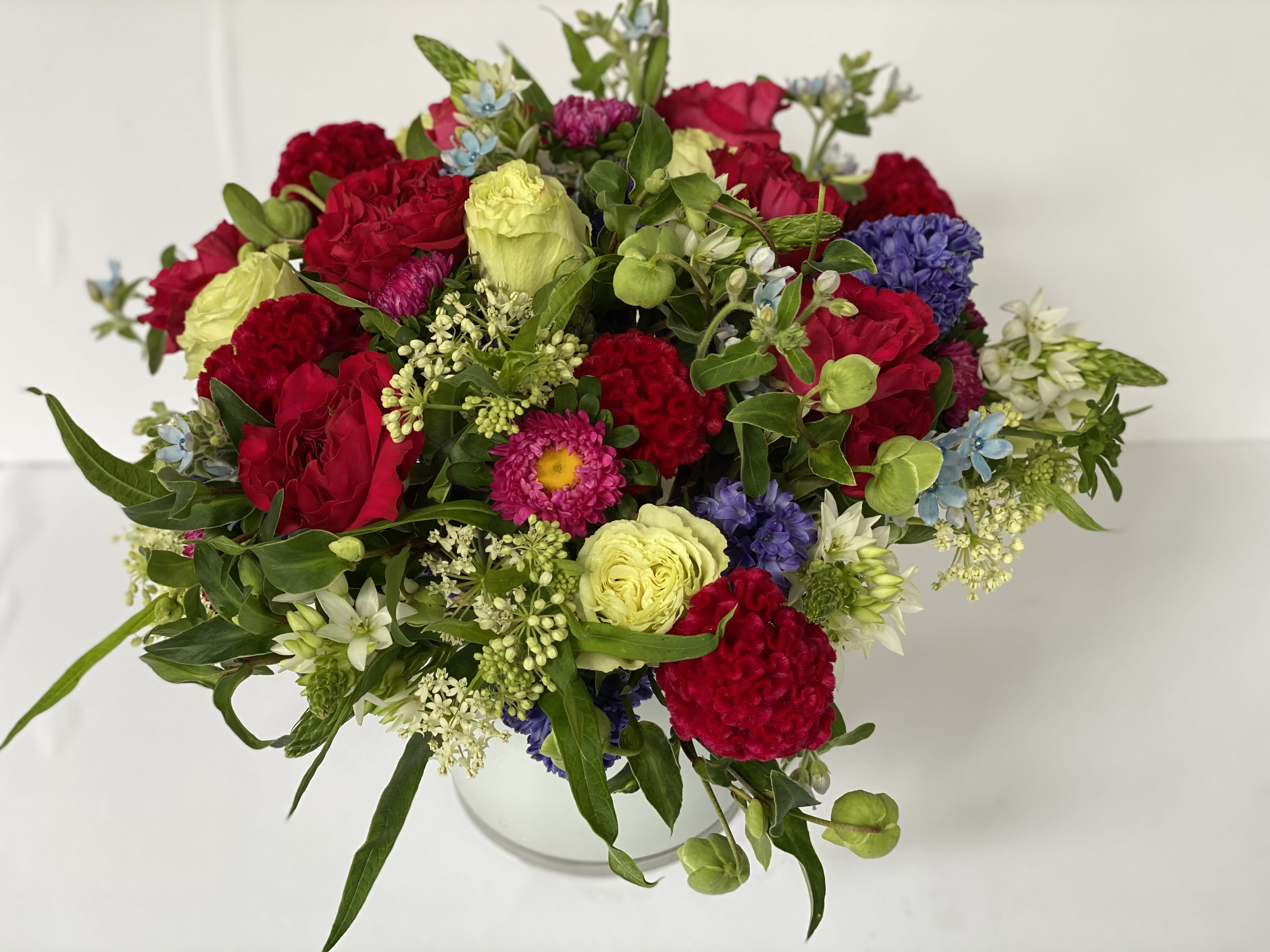 AUTUMN # 2 - LUSH ASSORTMENT OF GARDEN ROSES, LEMONADE ROSES, WINTER BELL HELLEBORE,  ASCLEPIAS ICE BALLET, TWEEDIA, HYACINTHS IN A LOW ROUND WHITE CYLINDER. 