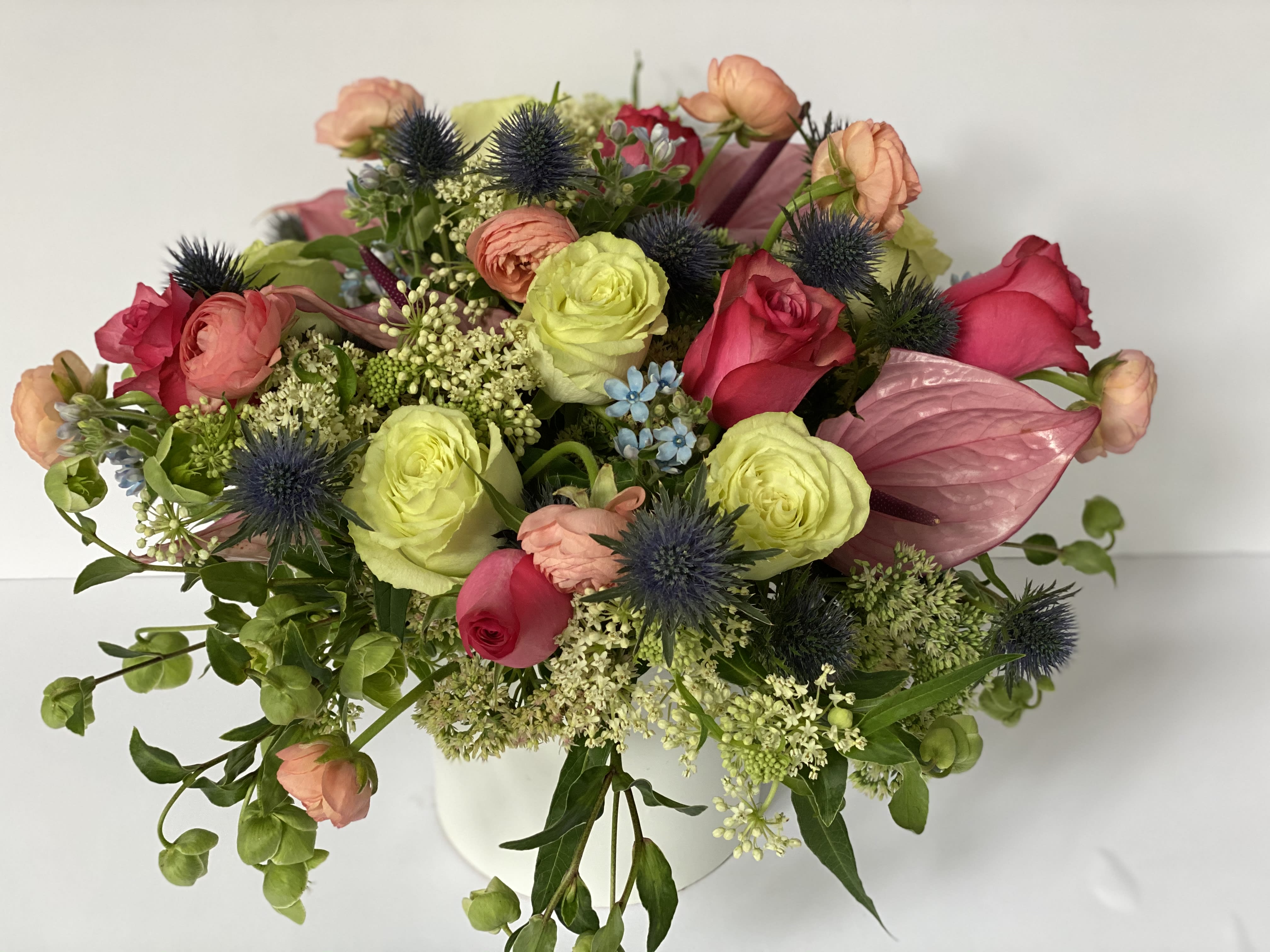 WINTER BELLS - This elegant arrangement,  complemented by swirling cherry roses, soft and subtle tweedia, and lemonade roses. Framed by lush autumn textures like apricot ranunculos, ruffled greenery, and lofty stems of hellebore winter bells  in a textured bowl.