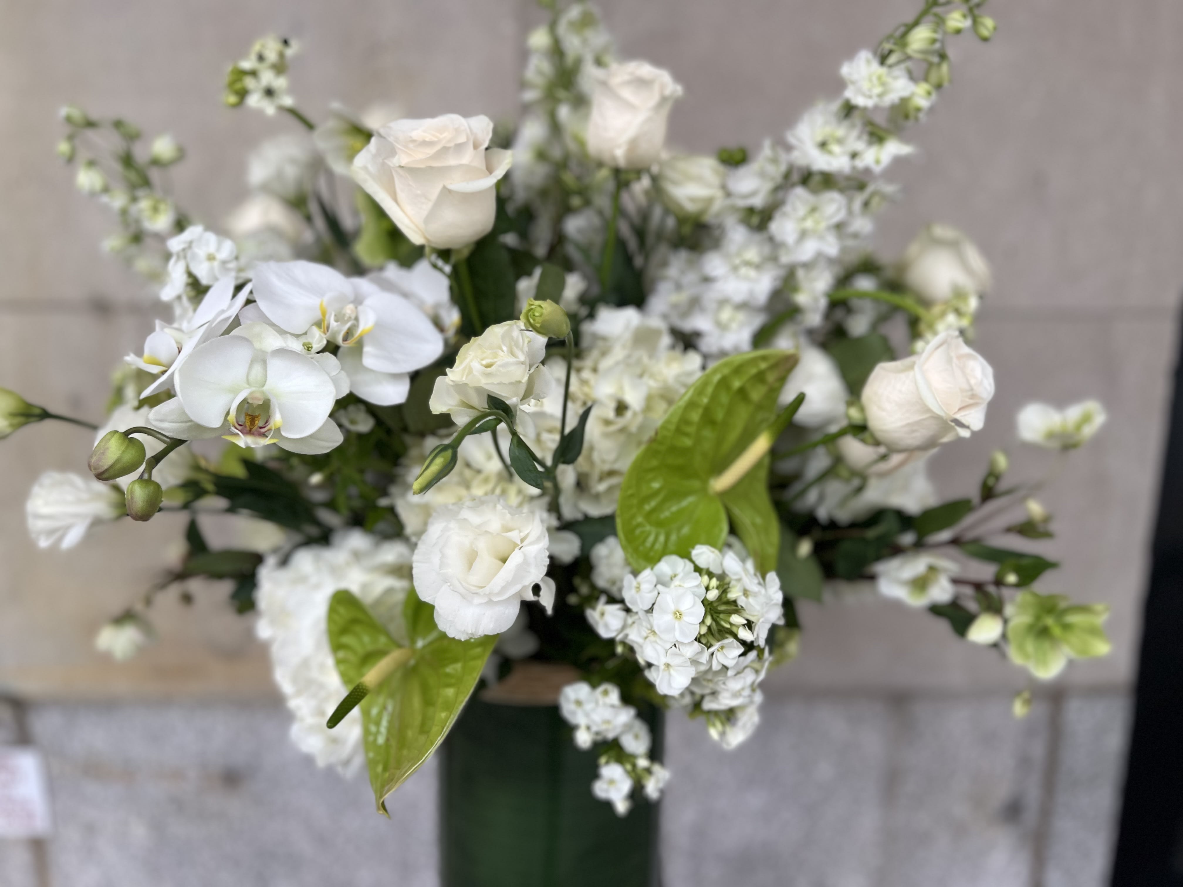 White floral arrangement with roses and orchids in a tall vase
