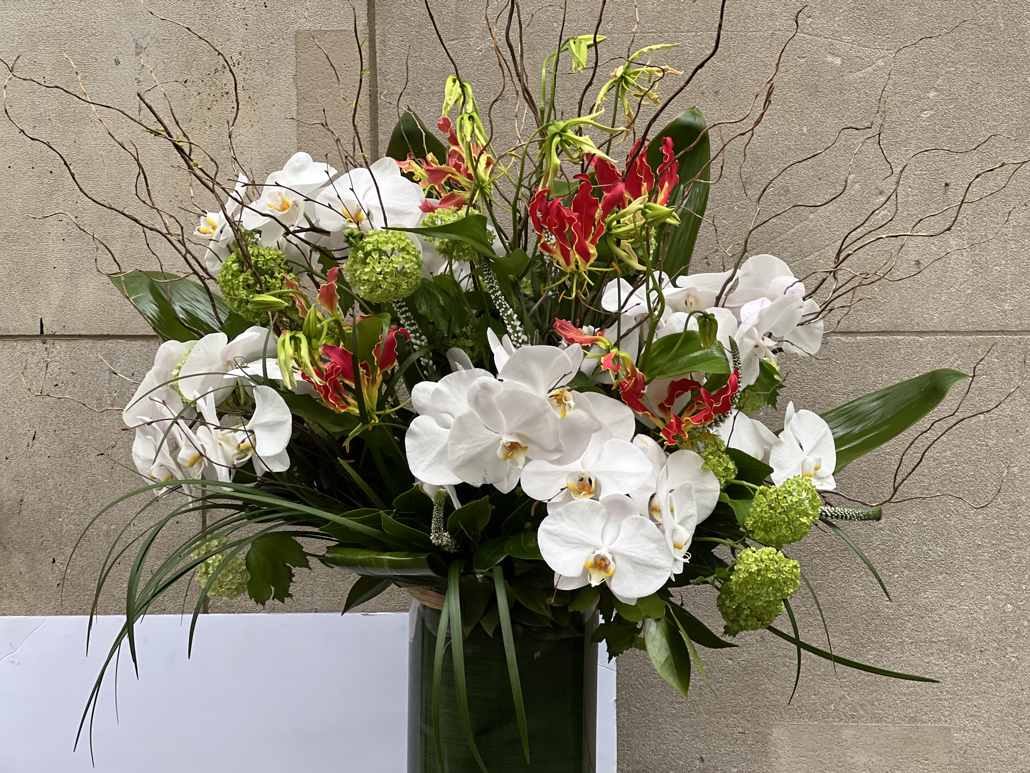 JAPANESE ARRANGEMENT 2 - CYLINDRICAL VASE WITH JAPANESE GLORIOSA, WHITE PHALAENOPSIS ORCHIDS, VIBURNUM, THAI LEAF, AND BEAR GRASS.