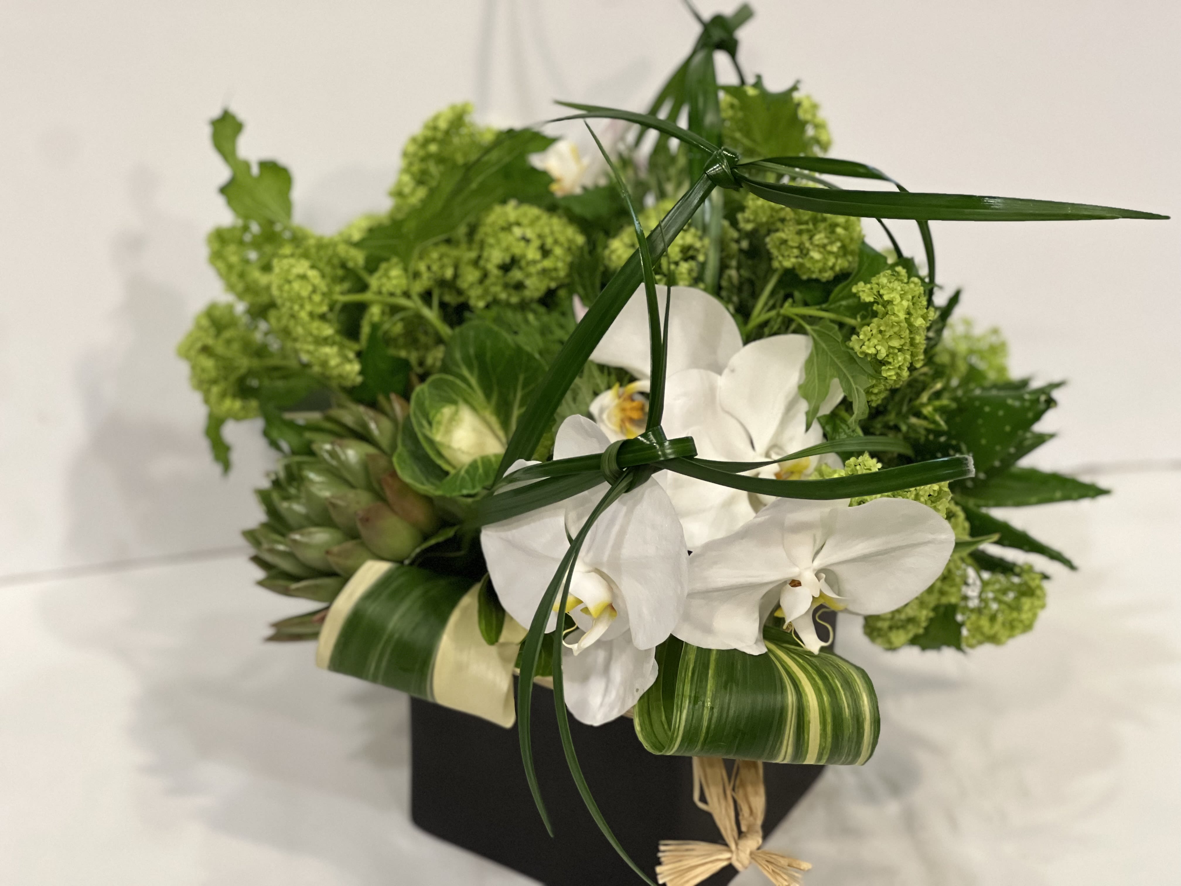 White orchids and green flowers in a black box arrangement