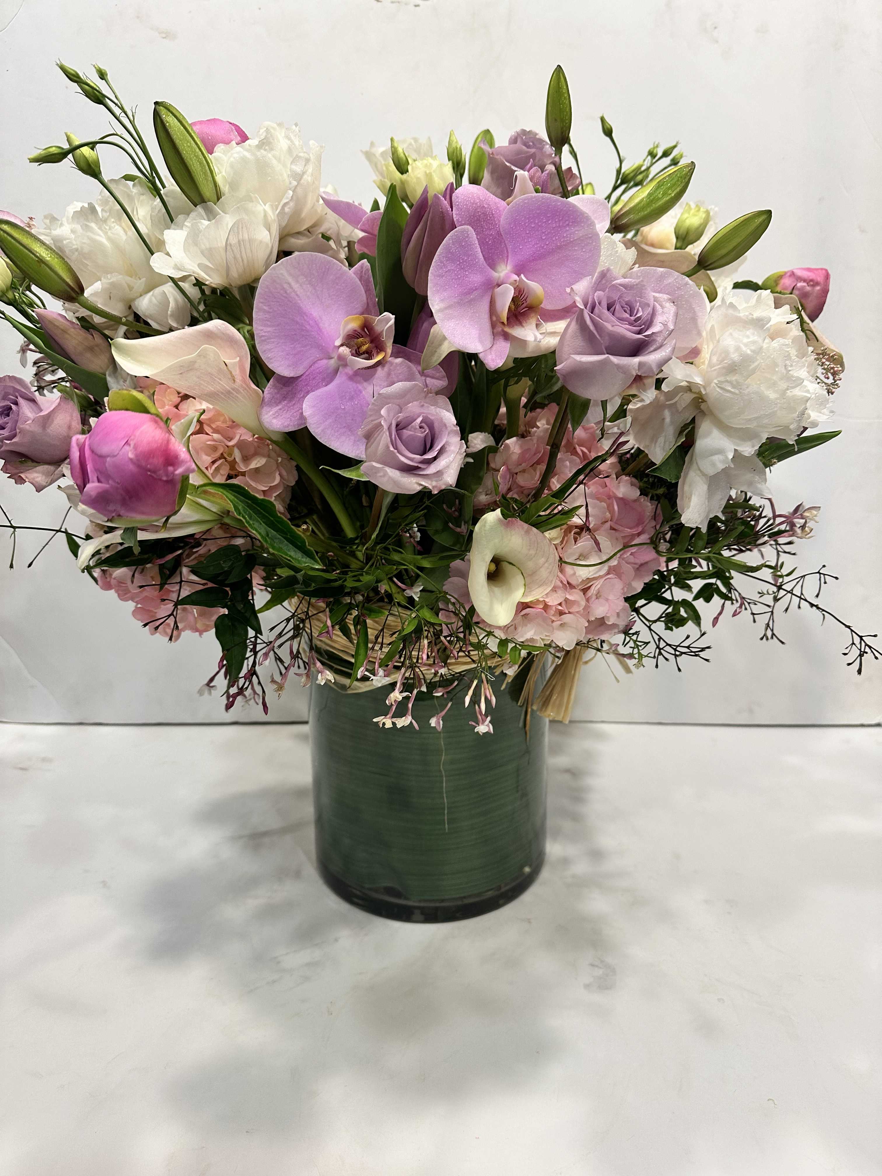 JULES ELIE - Medium high floral arrangement compose of an assortment of Jules Elie peonies, lavender phalaenopsis, Festiva maxima peonies, blush calla lily's, light pink hydrangeas, surrounded by jasmine and rice flowers from California farms. 