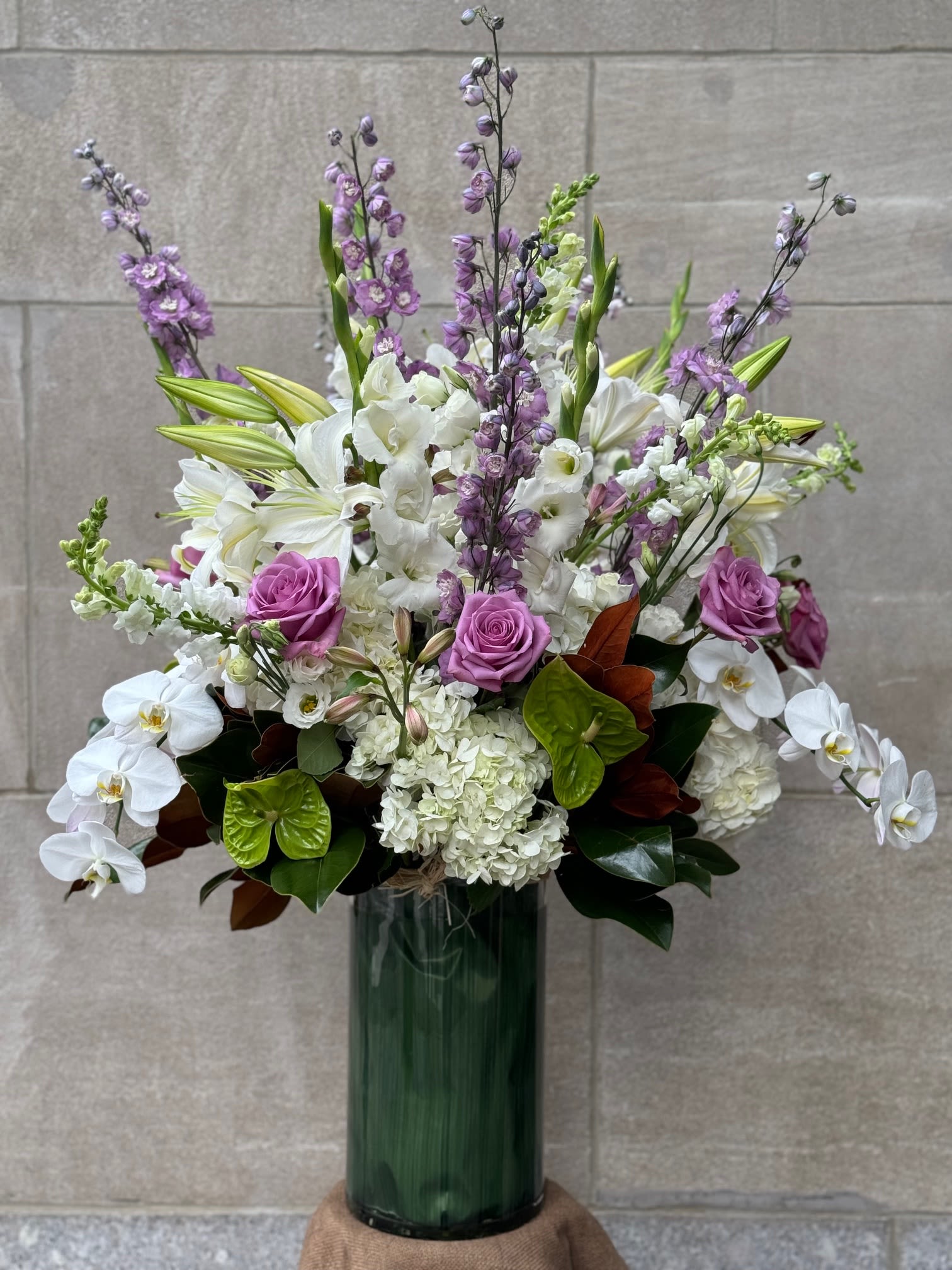 Tall bouquet of white orchids, lilies, hydrangeas, and purple roses in a glass vase
