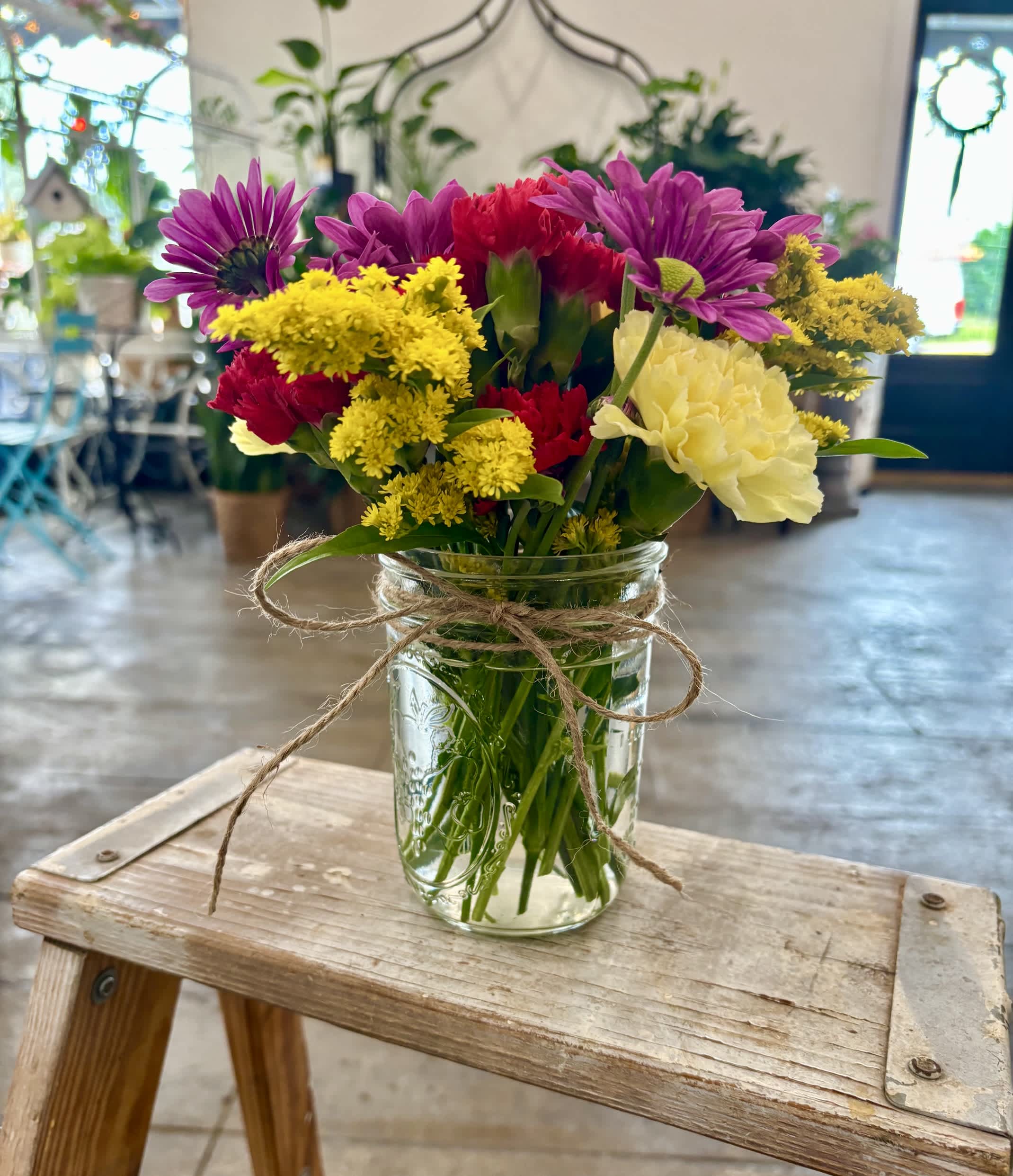 Mixed bouquet of purple, red, yellow, and white flowers in a glass jar vase