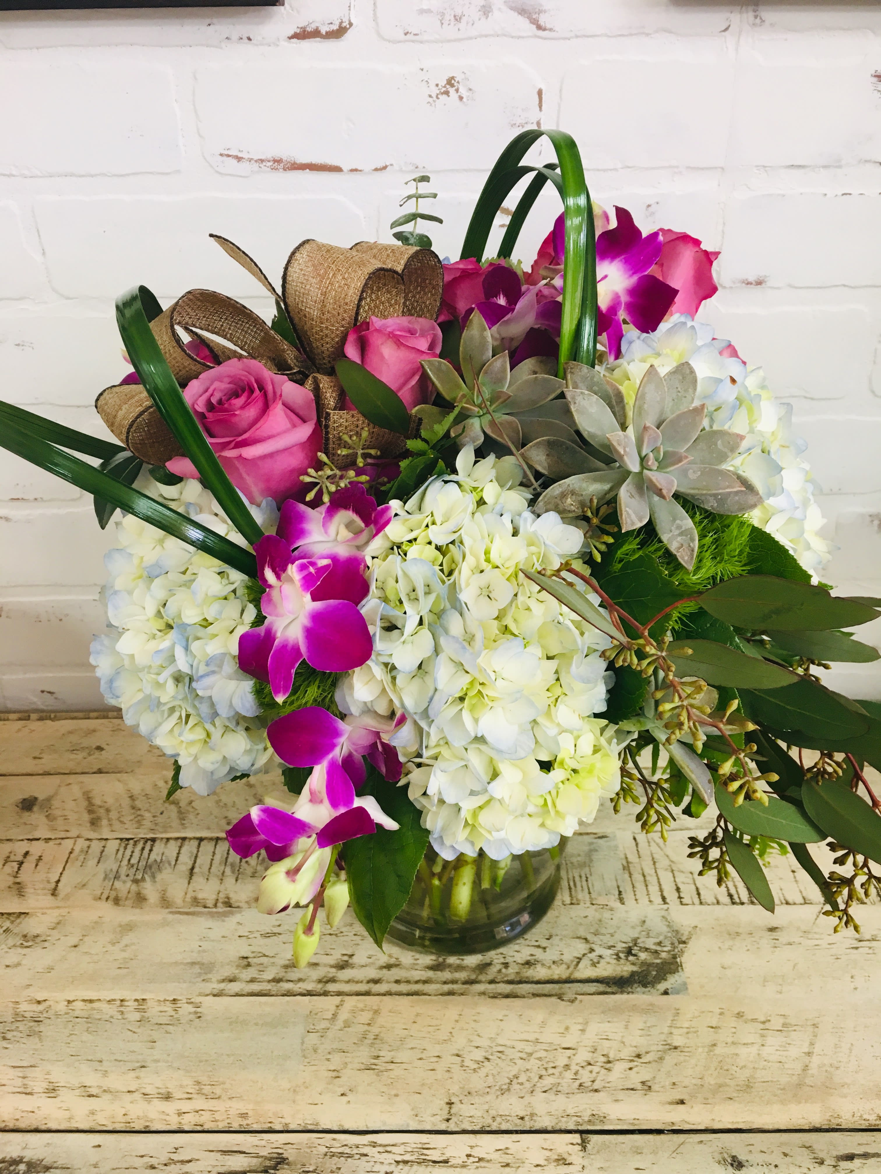 Pink roses and purple orchids arranged with white hydrangeas in a glass vase