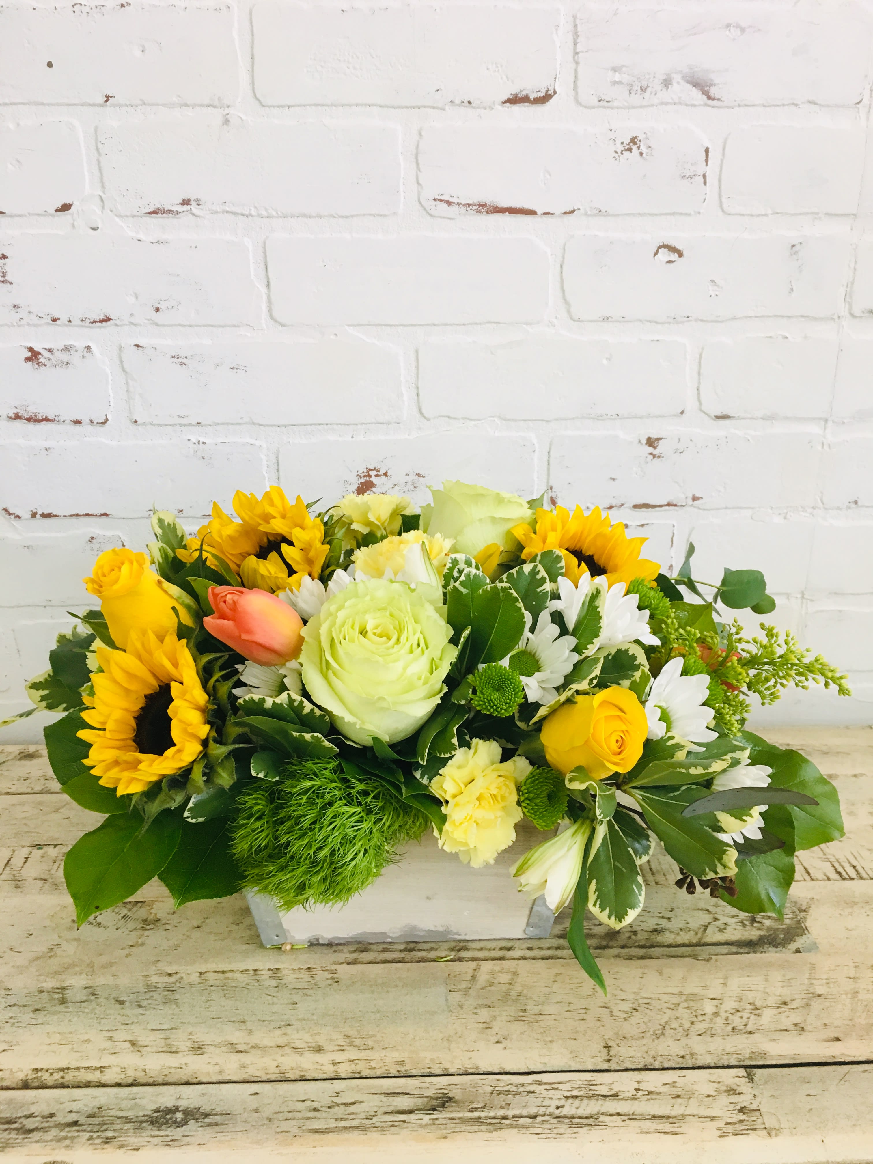 Low centerpiece of sunflowers, yellow roses, white daisies and green accents in a white wooden box.