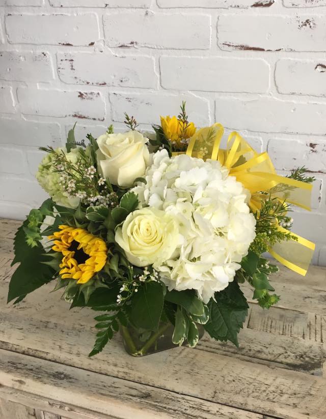 Bouquet of white roses, hydrangea, and sunflowers in a glass vase with yellow ribbon