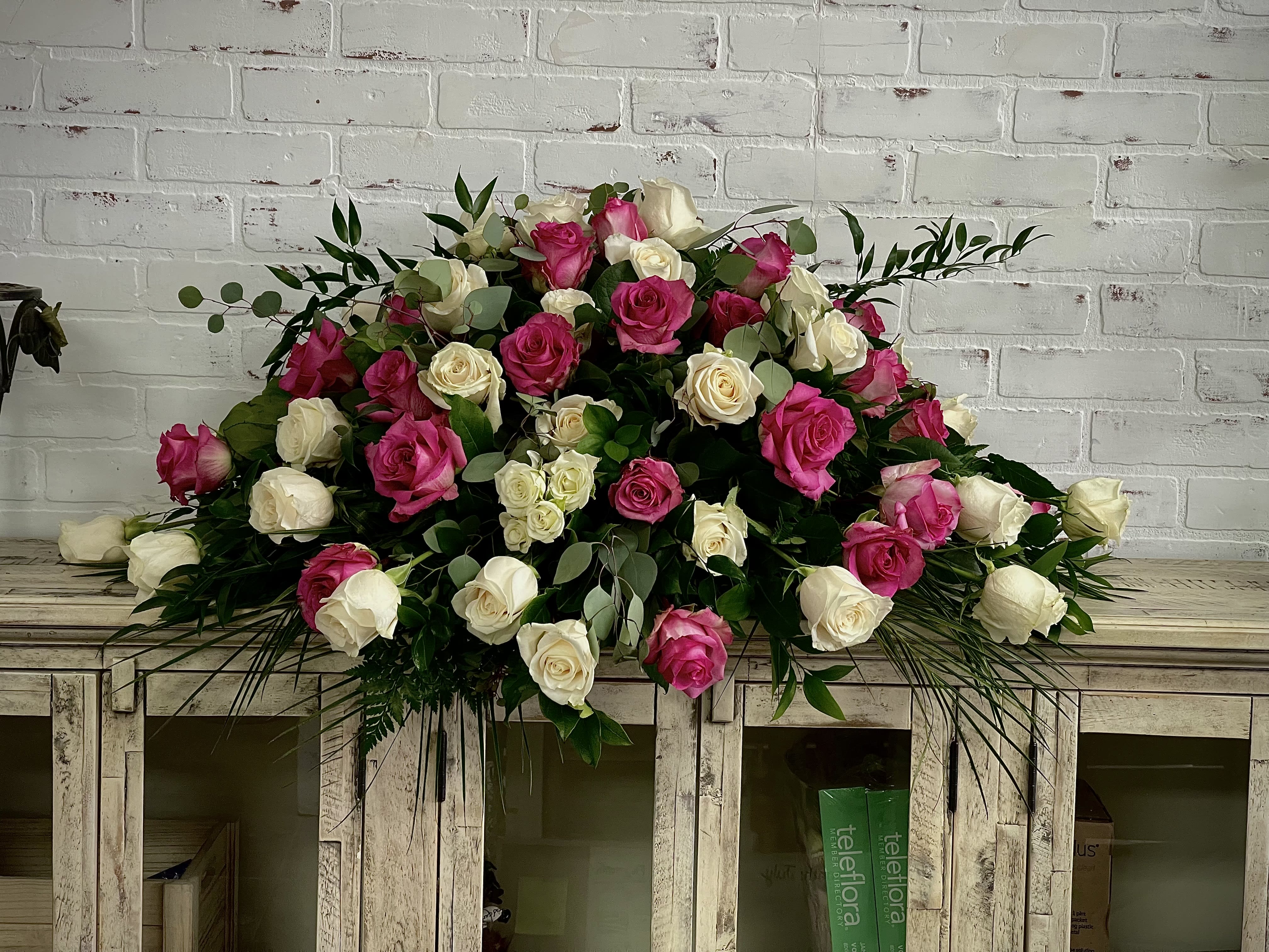 Large bouquet of pink and white roses with greenery on a wooden cabinet