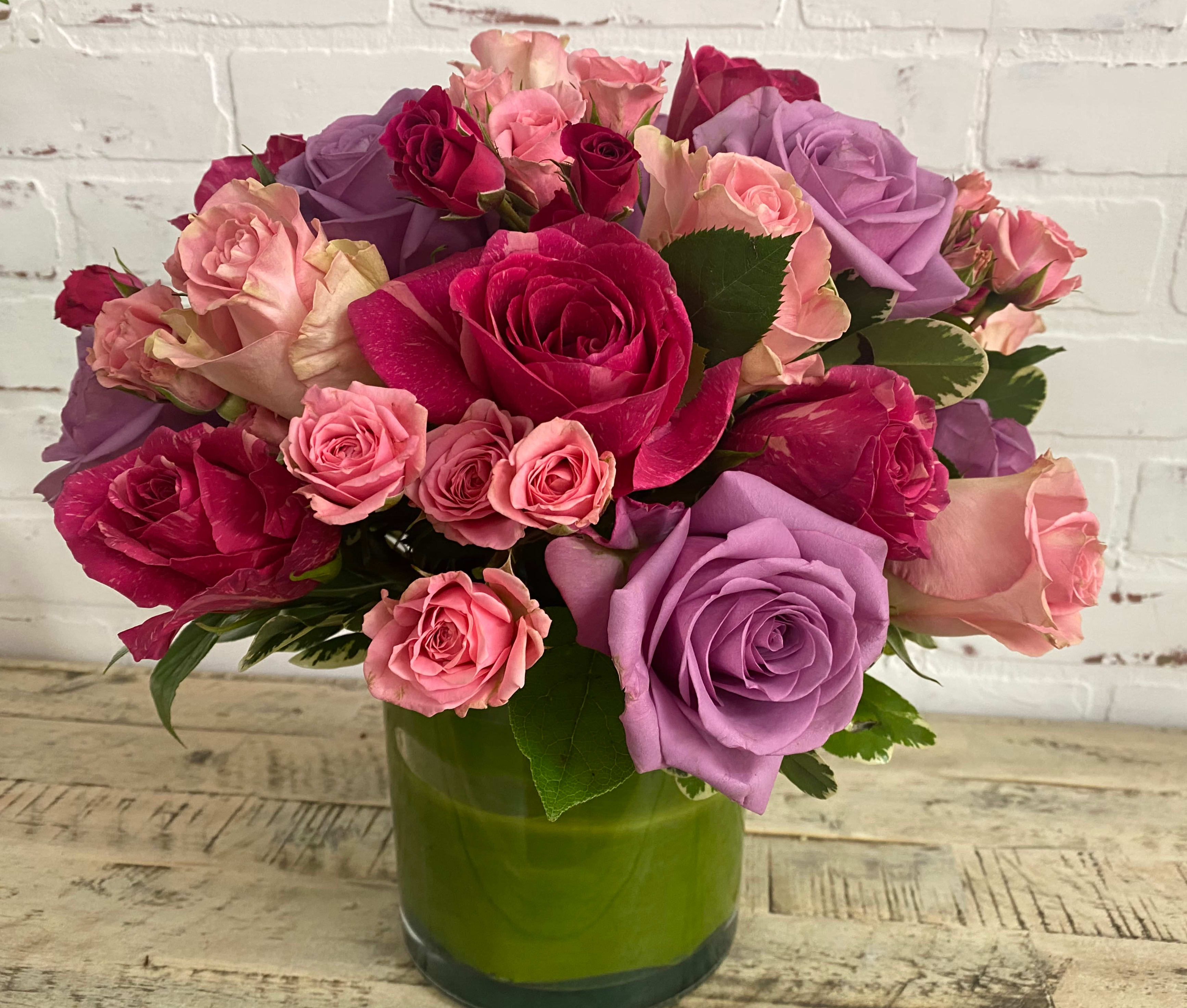 Bouquet of pink, purple, and red roses in a green glass vase