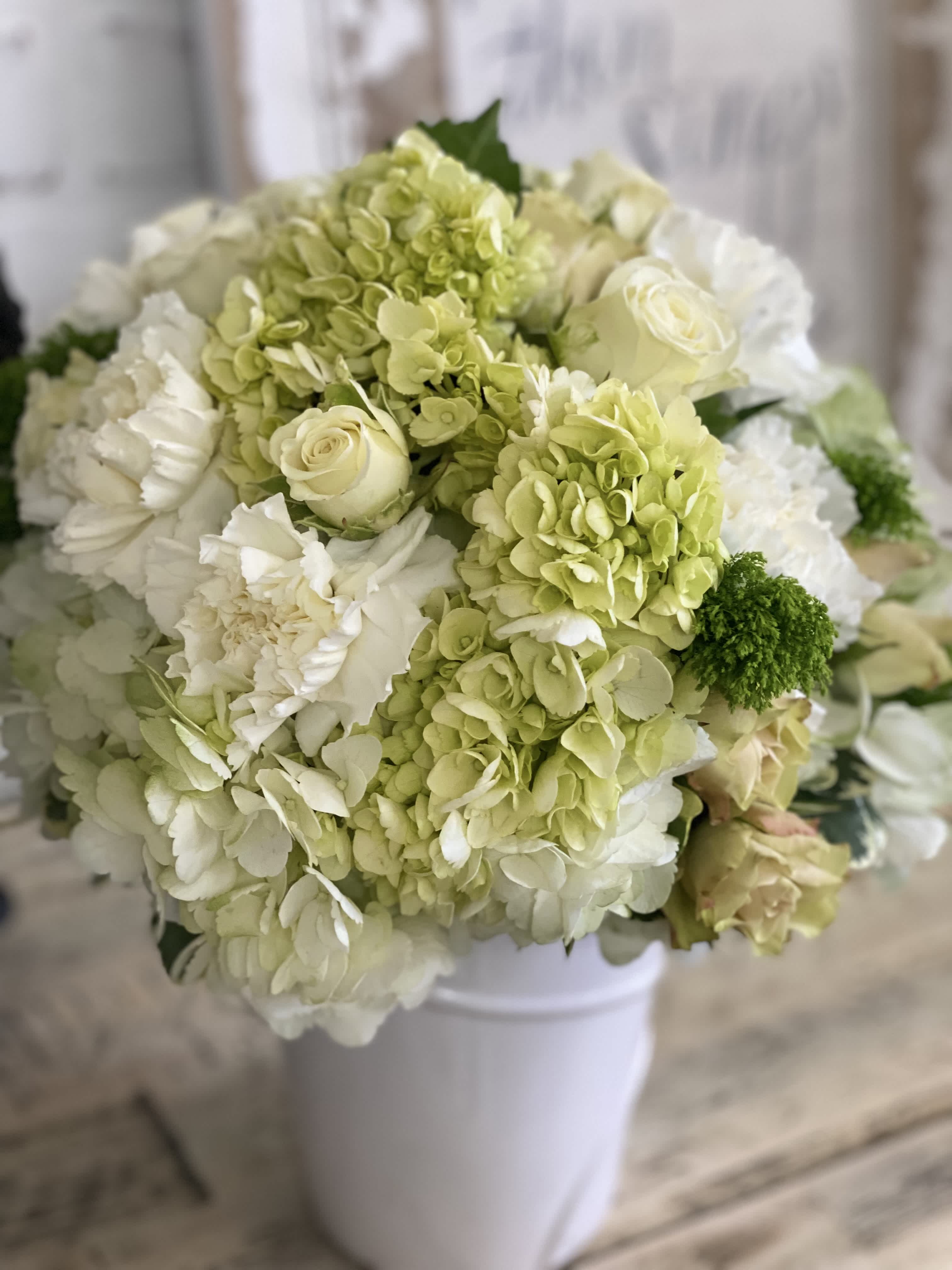 Round arrangement of white and pale green hydrangeas, roses, and carnations in a white vase